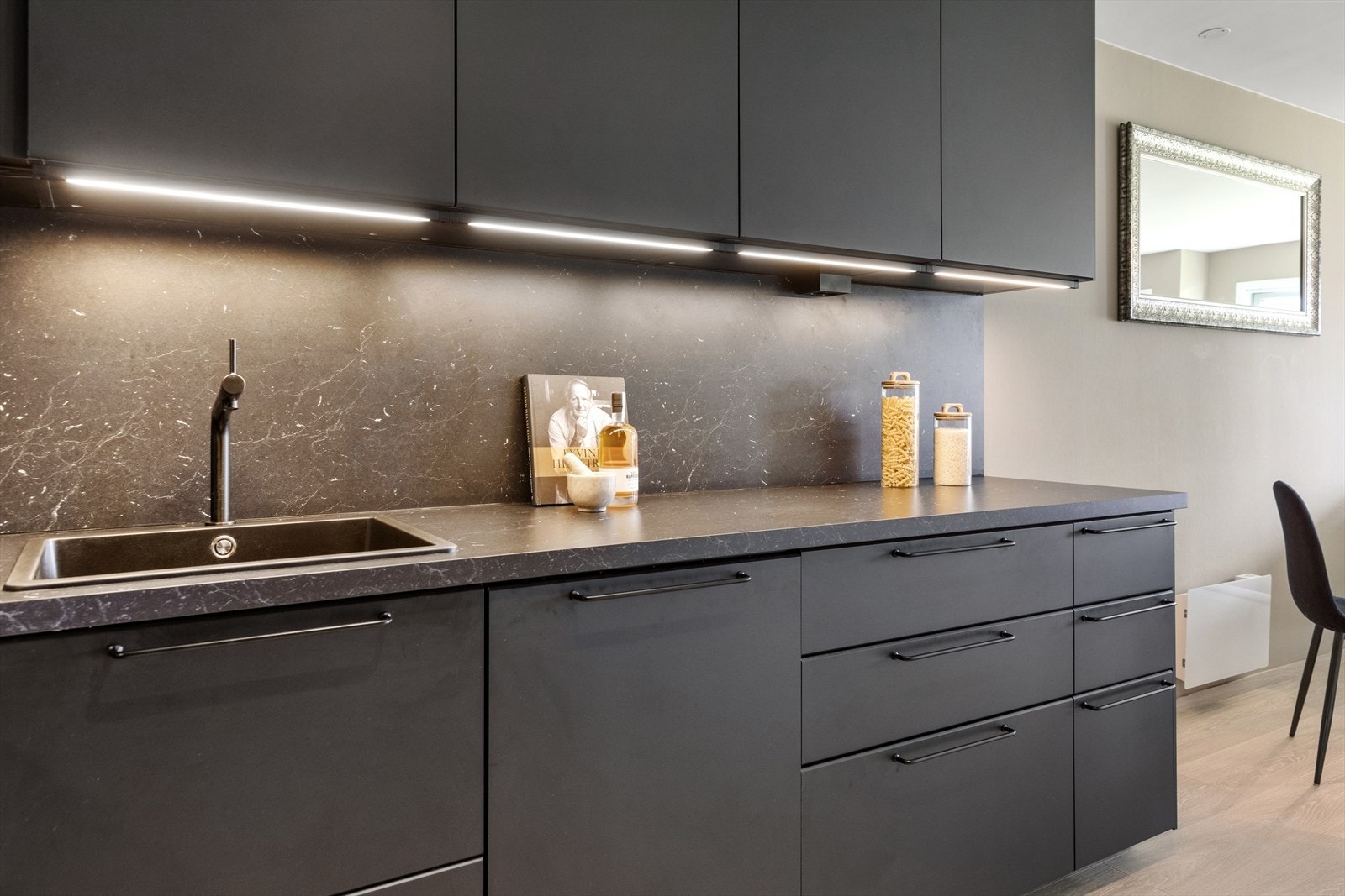 Oppvaskkummene er i sort kompositt med sort kran. Hvitevarene består av koketopp, stekeovn, oppvaskmaskin og kjøl/frys. Galleribilde