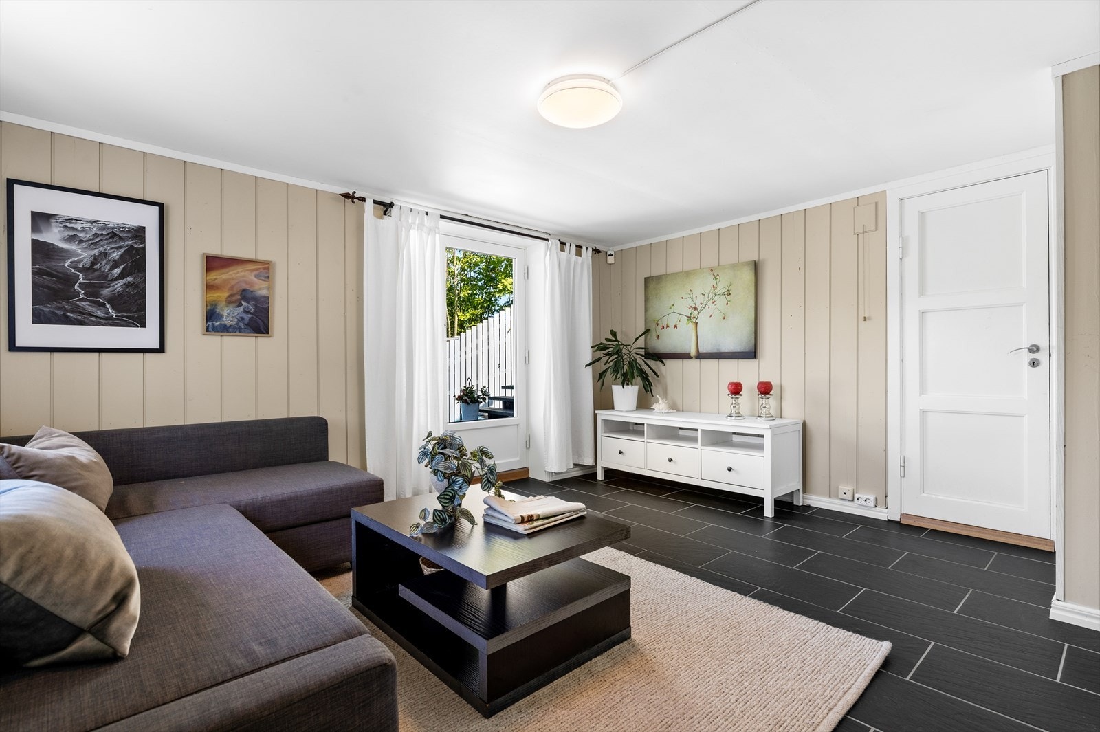 Lys og romslig kjellerstue med fliser på gulv. Her er det plass til sofagruppe, kontor, treningsapparater m.m. To boder til høyre i bildet. Galleribilde