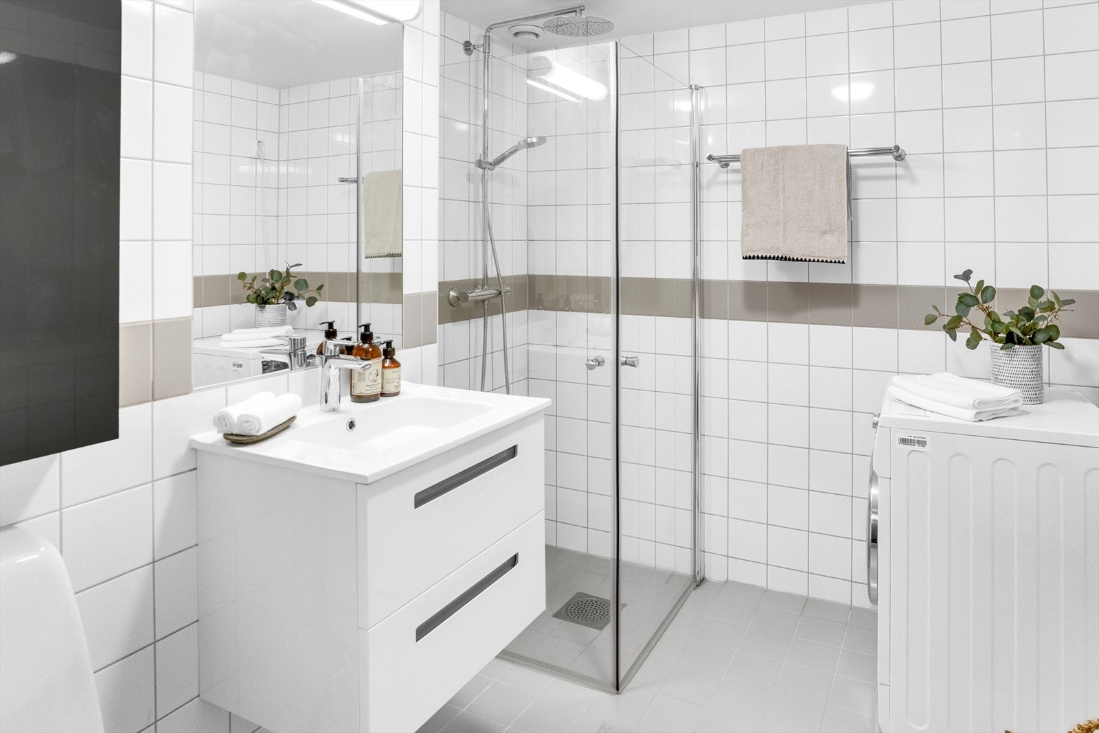 Badet inneholder veggskap, wc, servant med skuffer, speil med lys, dusjhjørne med regndusj og glassdører samt opplegg for vaskemaskin. Galleribilde