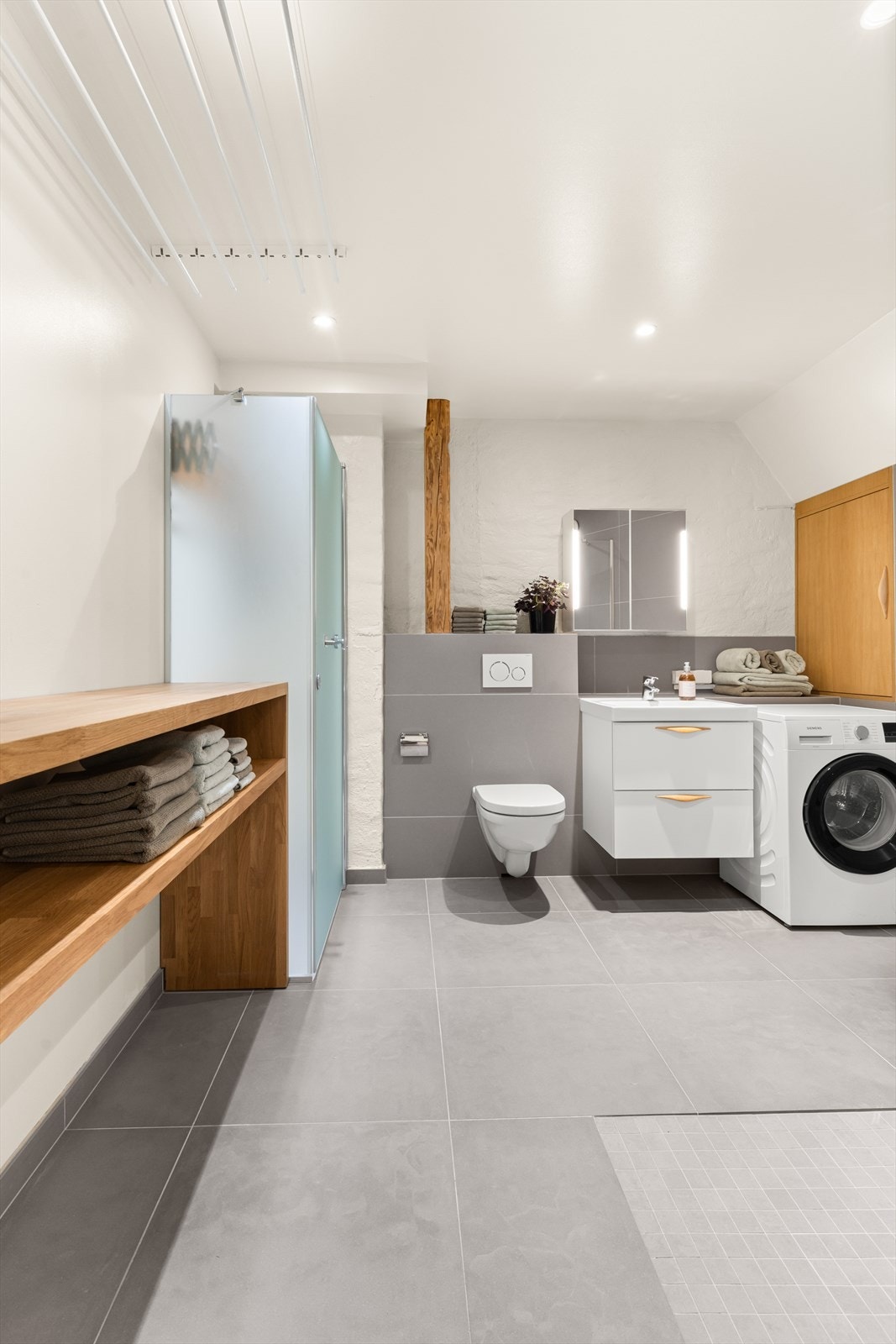 Det største badet er kombinert vaskerom og bad. Her er det plassbygget strykebenk og hylle i eik, med plass til oppbevaring. Badet har en egen, stor varmtvannstank skjult i et skap med eikedør i badets endevegg. Galleribilde