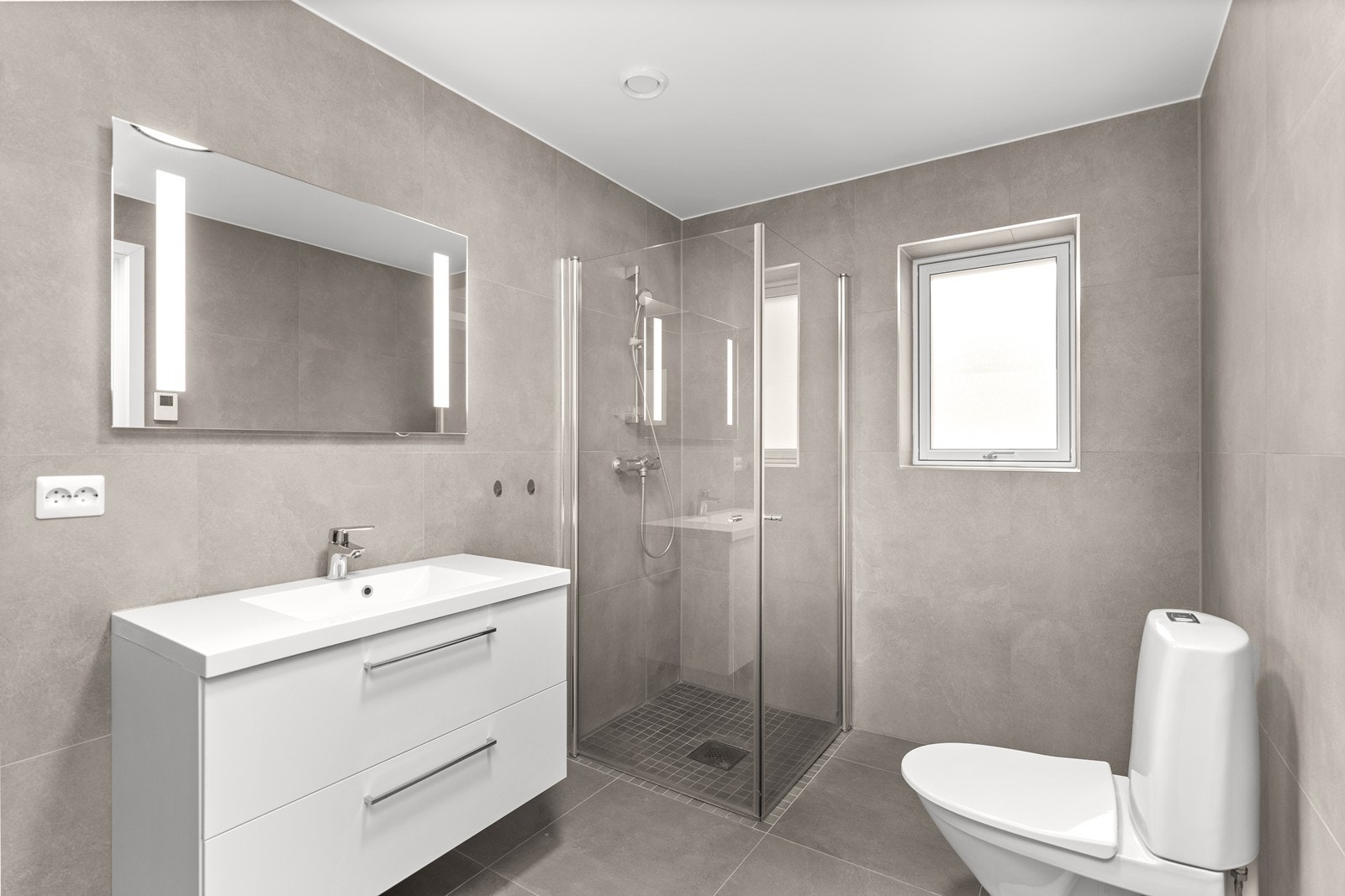 Baderom er innredet med dusj på gulv. servant med romslige skuffer og wc. Galleribilde