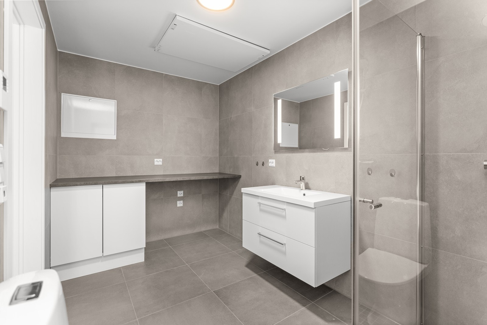 Pent bad med 60x60 fliser på gulv. Varmekabler i gulv og opplegg/ plass til både vaskemaskin og tørketrommel under benk. Galleribilde