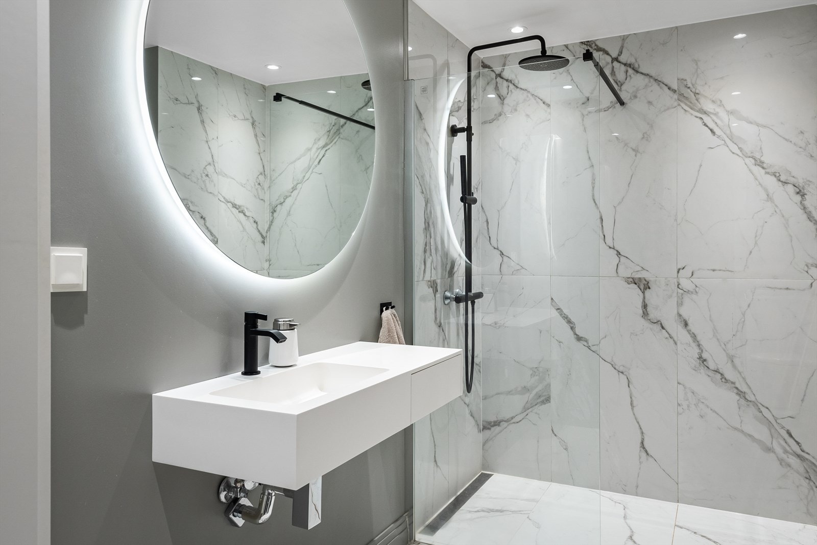 Baderommet har et moderne og tiltalende uttrykk med lys marmorflis og stramme sorte detaljer. Galleribilde