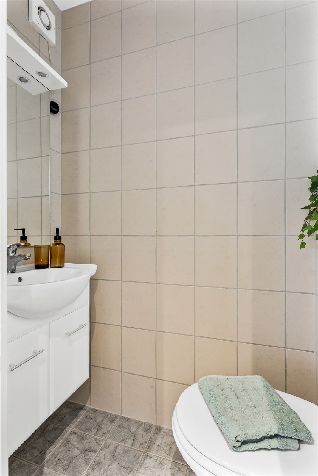 Rett innenfor døren er det et separat, flislagt wc-rom/gjestetoalett med vegghengt wc og servant med underskap, speil og belysning. Galleribilde