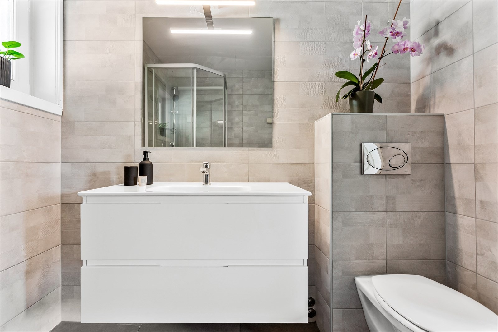 Moderne, flislagte bad meed vegghengt wc, servant i hvit skuffeseksjon med speil over. Galleribilde