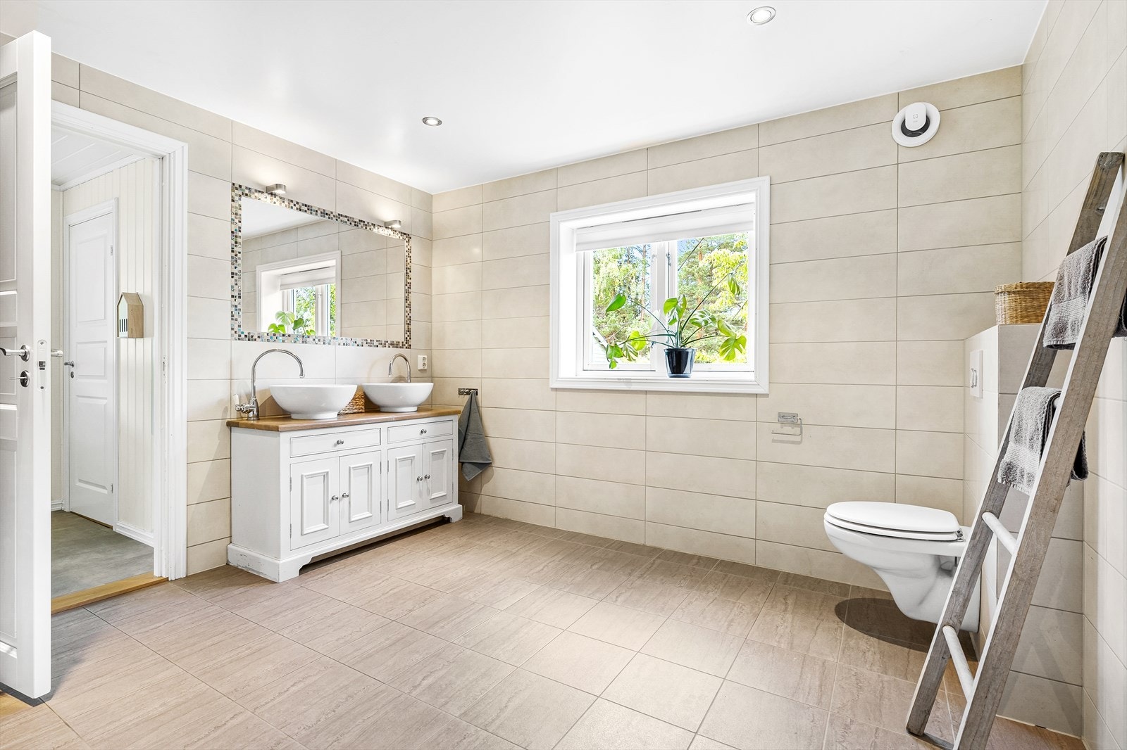 Badet er innredet med et flott servantskap med dobbel servant, vegghengt toalett med skjult sisterne og et stort dusjhjørne med mosaikkfliser og rengfallsdusj Galleribilde