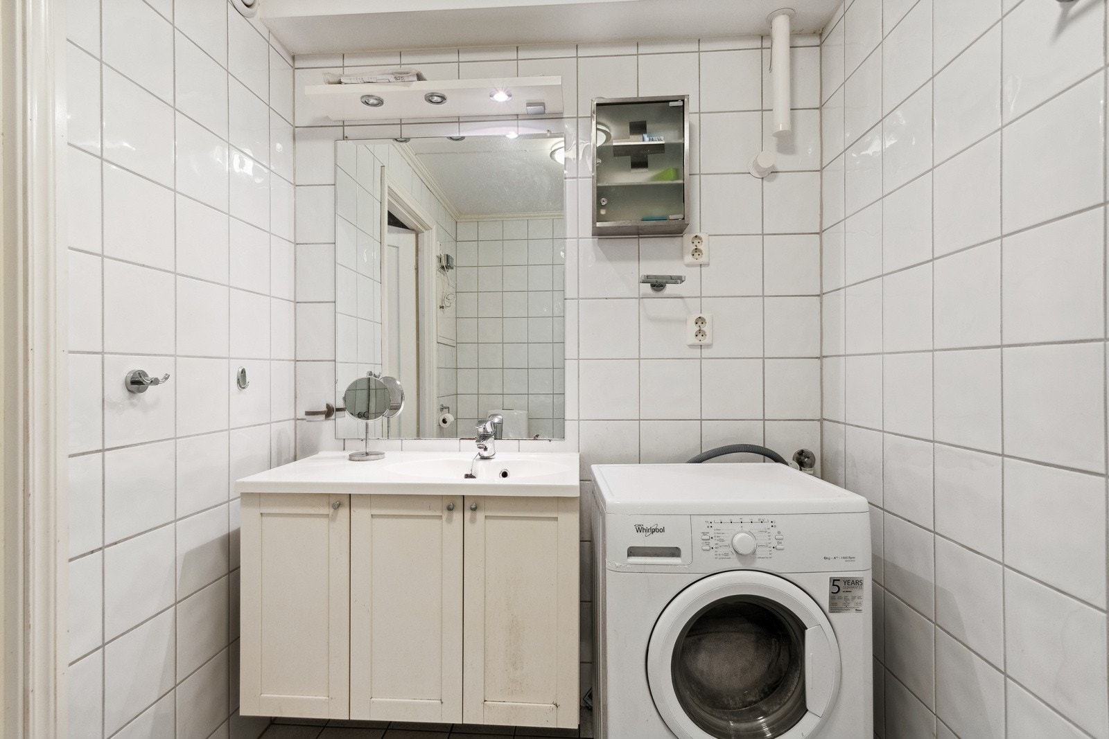 Flislagt baderom bestående av toalett, dusjhjørne, servantinnredning og opplegg for vaskemaskin. Galleribilde