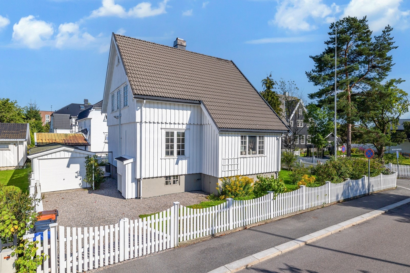 Tomten rammes fint inn av et hvitmalt gjerde med to doble porter ut til veien. Galleribilde