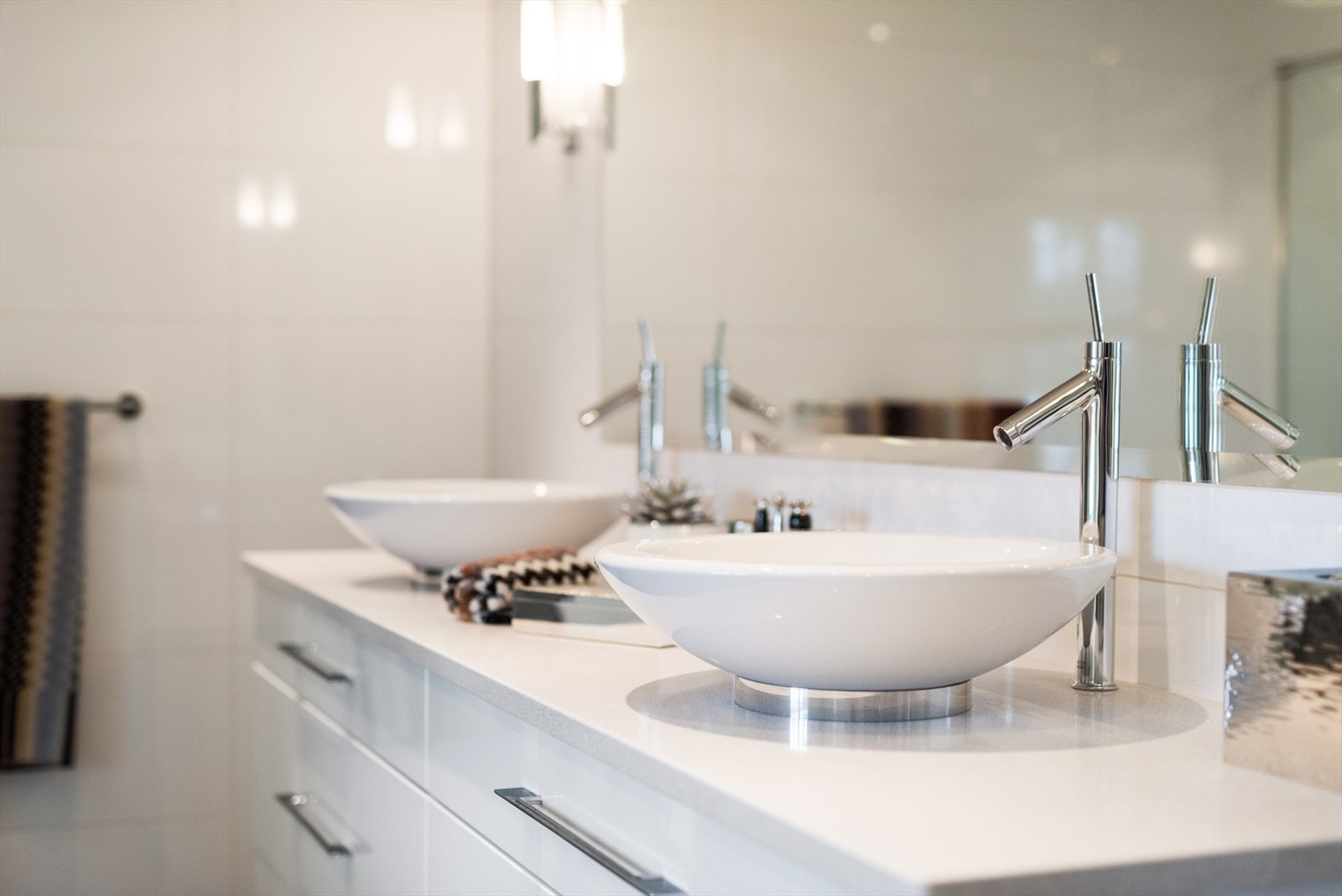 Innredningen har to toppmonterte servanter på granitt benkeplate, servantmøblement med hvite skuffefronter og belysning på hver side av et fasettslipt speil. Galleribilde