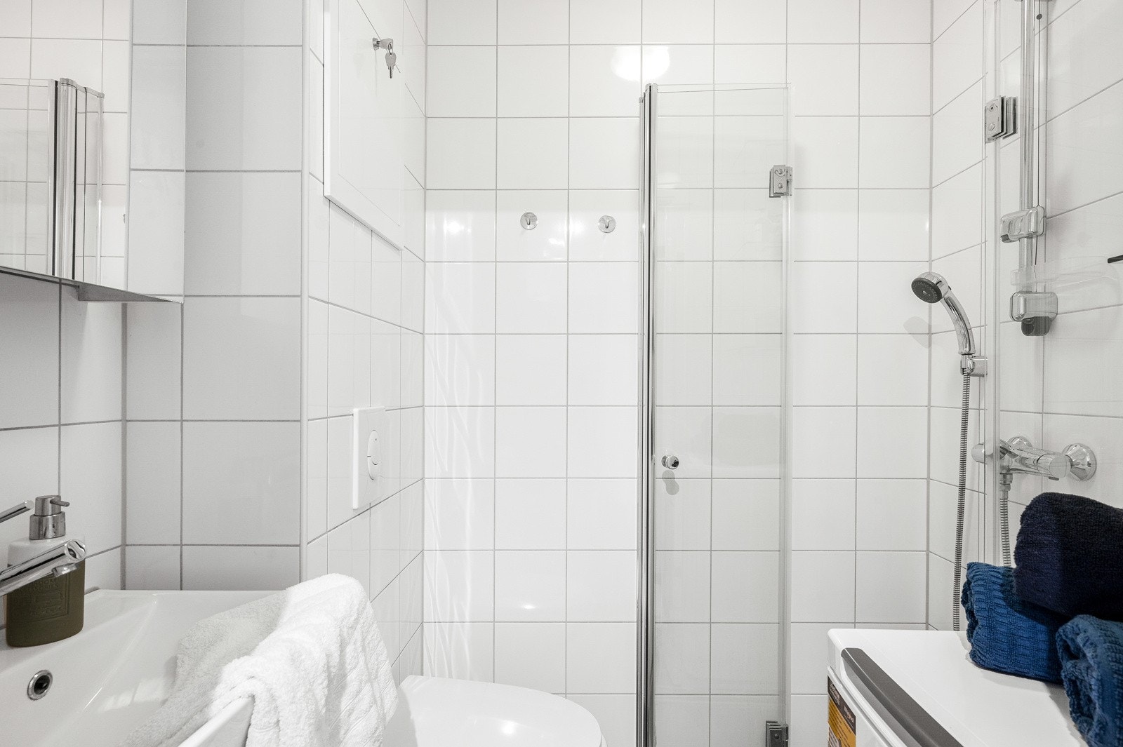 Pent oppusset bad i regi av borettslaget fra 2015, bestående av veggmontert toalett, opplegg for vaskemaskin og dusjhjørne med dører i herdet glass. Galleribilde