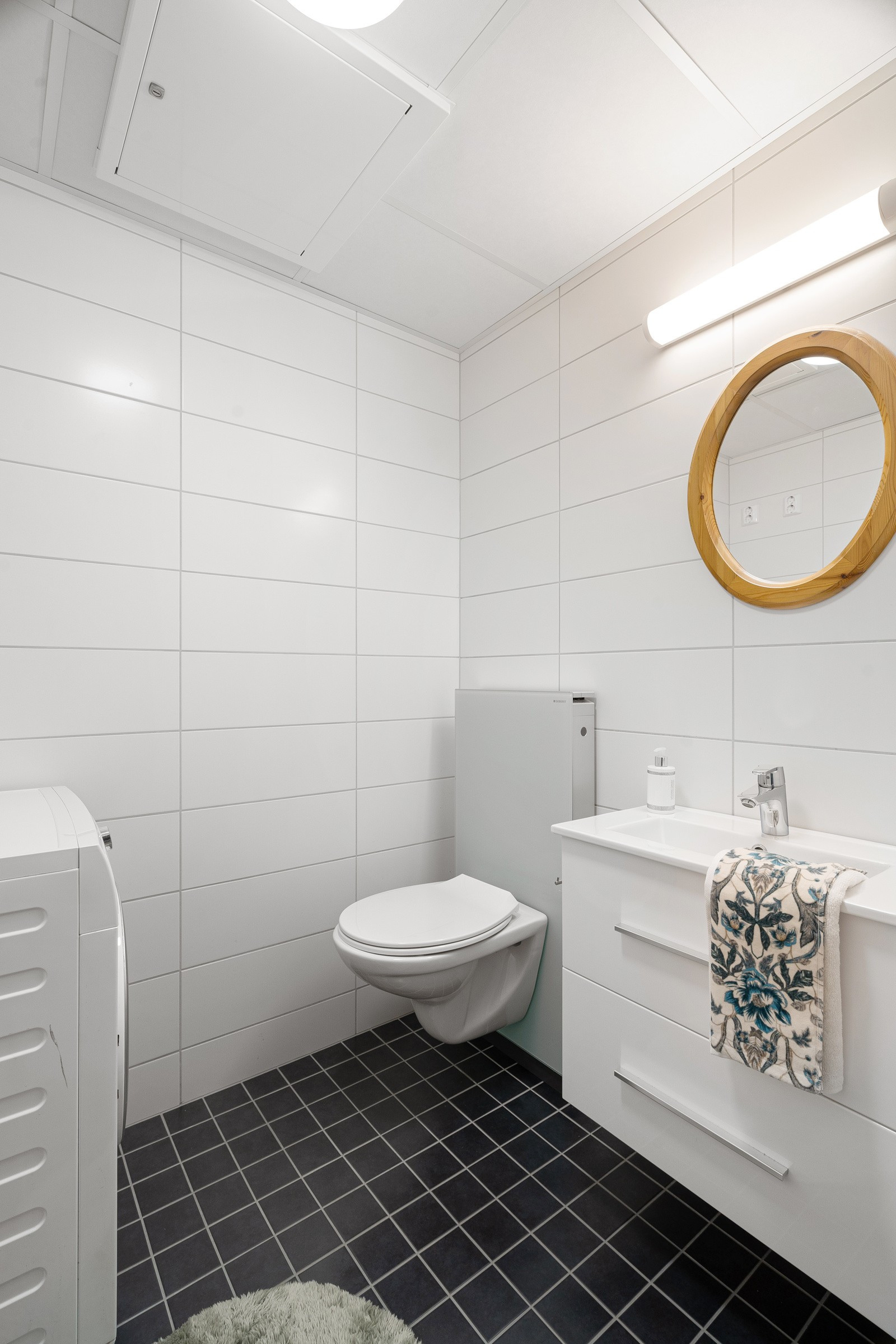 Praktisk vaskerom med vaskemaskin, toalett og baderomsinnredning.