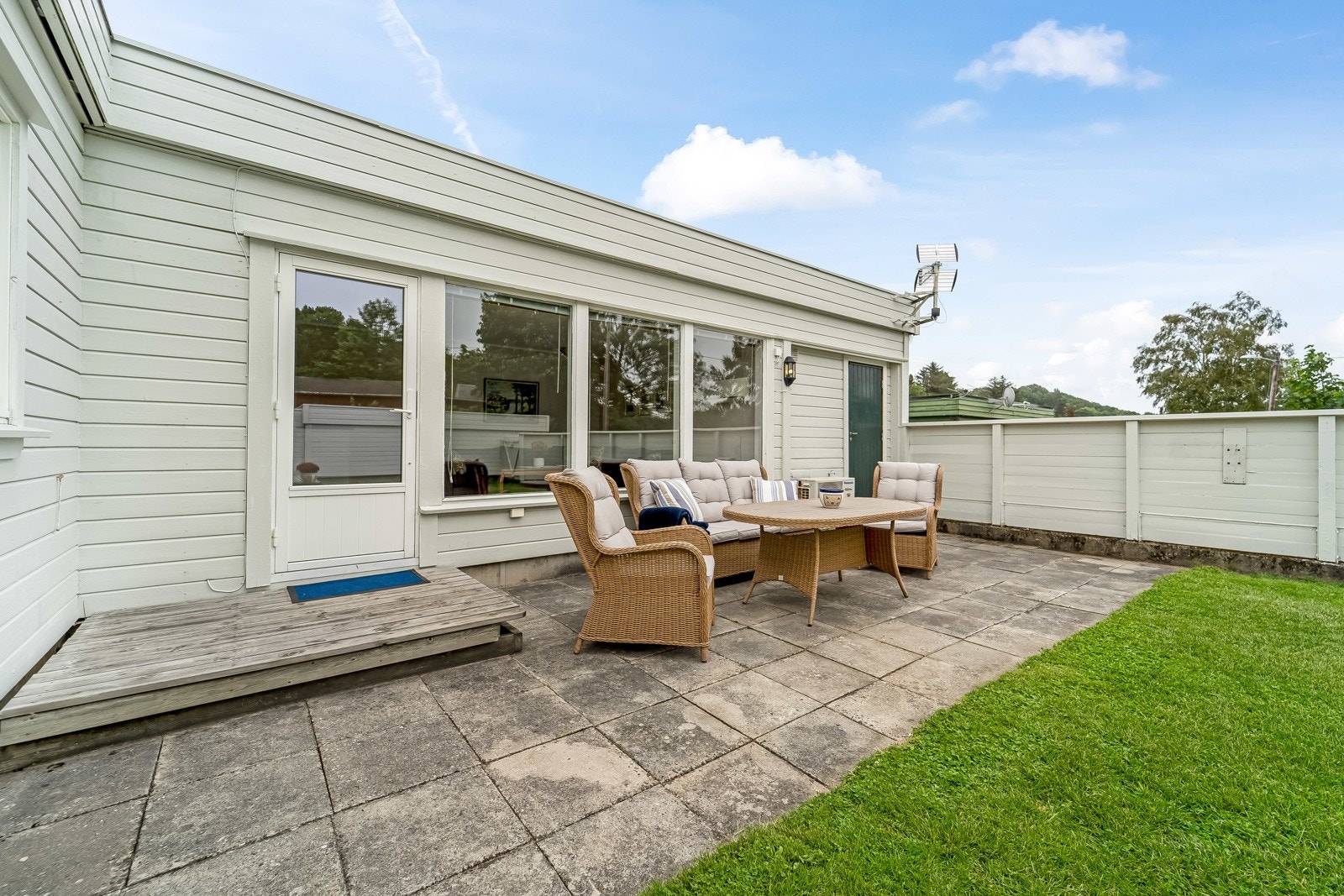 Terrasse belagt med heller ved stua. Adkomst til utvendig bod i enden. Galleribilde