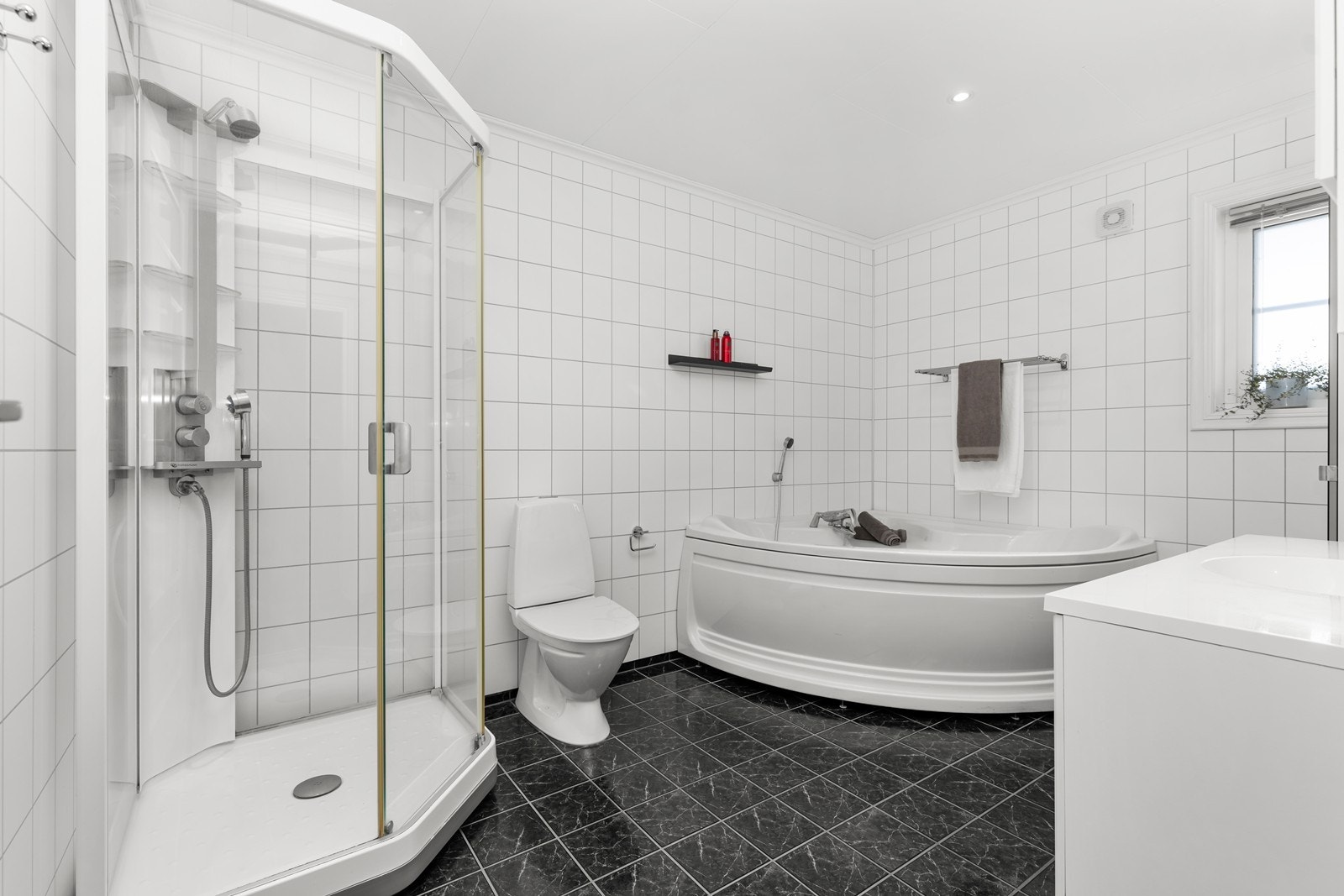 Badet har flislagt gulv og våtromsplater på vegger. Her er det stort hjørnebadekar, innredning med nedfelt servant, dusjkabinett og wc. Galleribilde