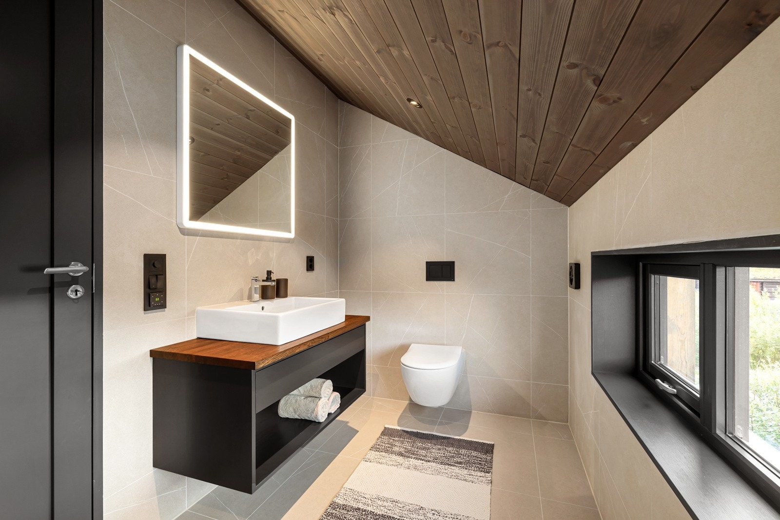 Badet har dusjhjørne, innredning med servant, speil med belysning og vegghengt toalett. Galleribilde