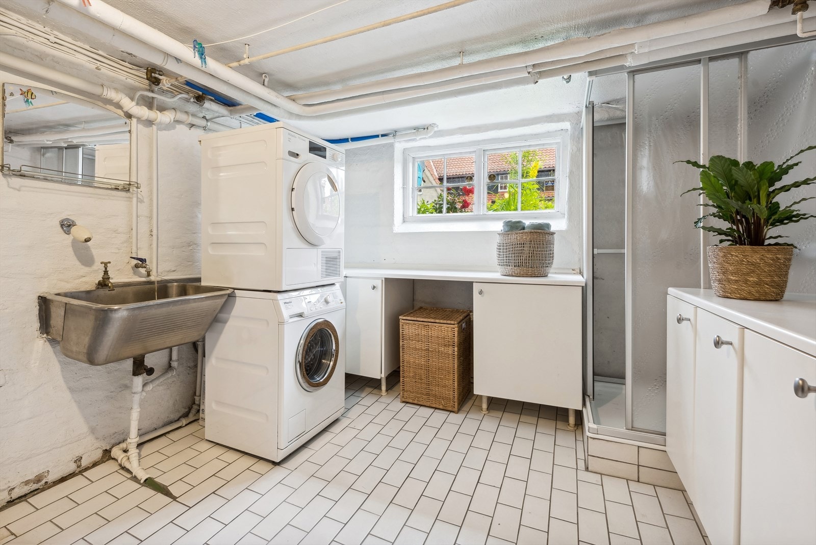 Et praktisk vaskerom i kjeller med dusjkabinett, skapinnredning, utslagsvask og opplegg for vaskemaskin og tørketrommel. Galleribilde