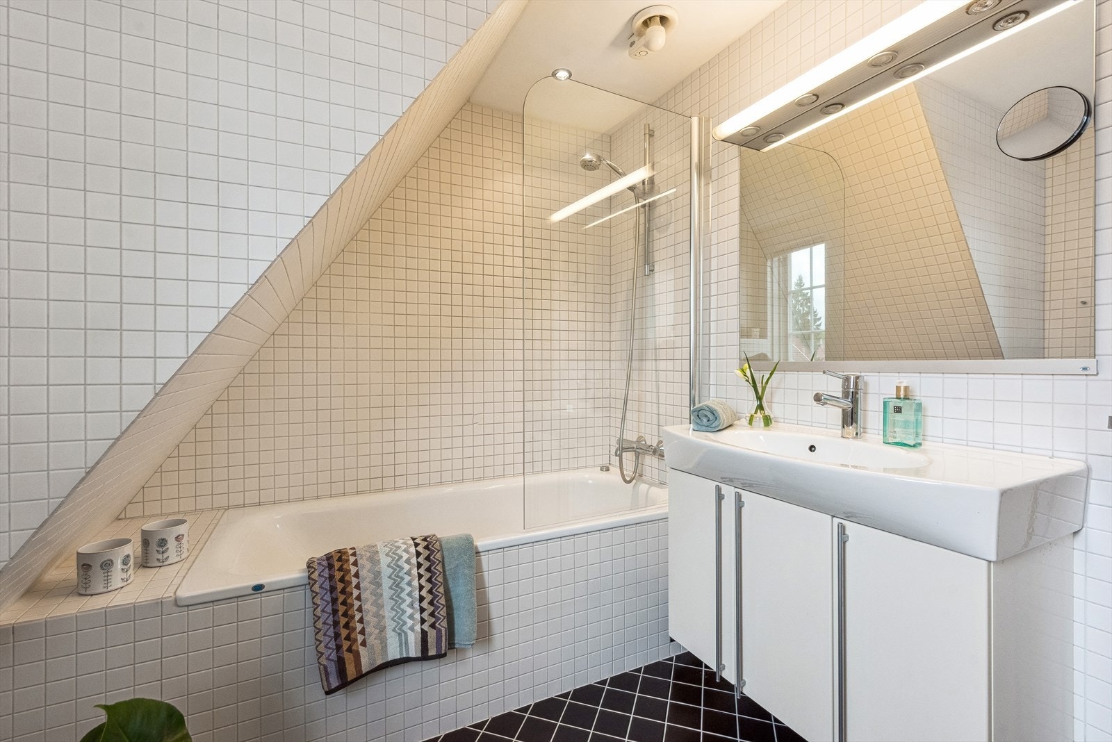 Et delikat flislagt dusjbad med badekar, vask med skap og speil, samt WC. Galleribilde