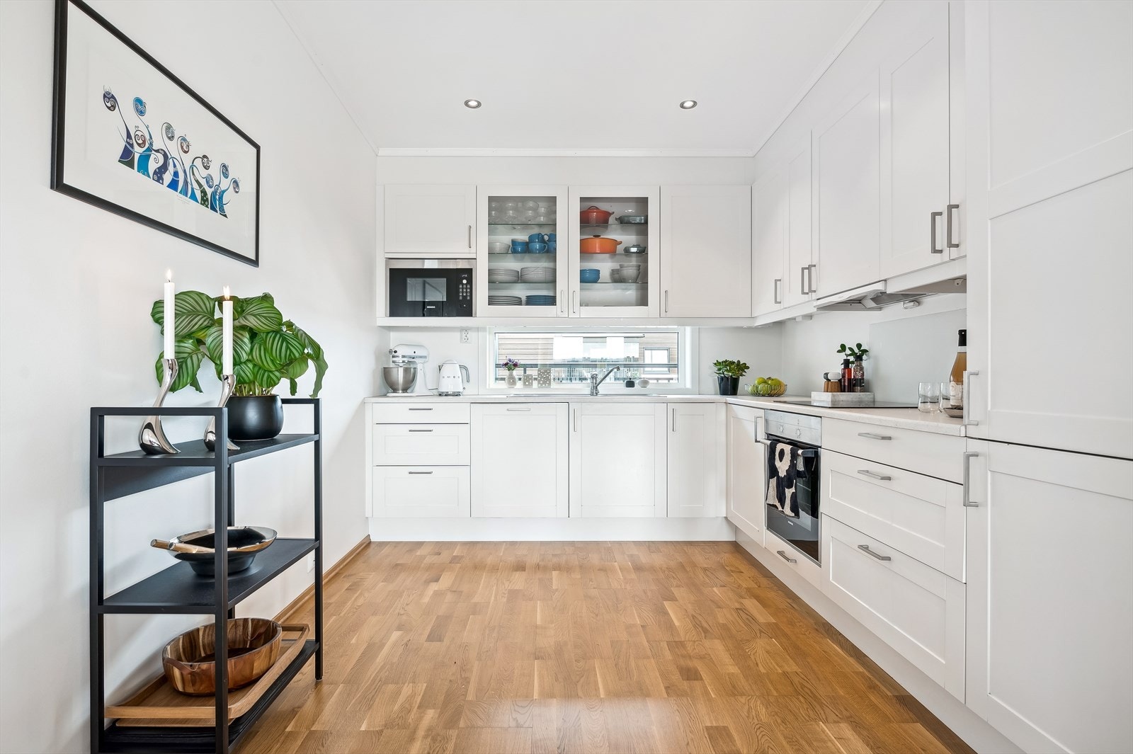 Kjøkkeninnredning med profilerte fronter, enkelte glassfronter i overskap, belysning under overskap, ventilator og laminat benkeplate med nedfelt kum i rustfritt stål. Galleribilde