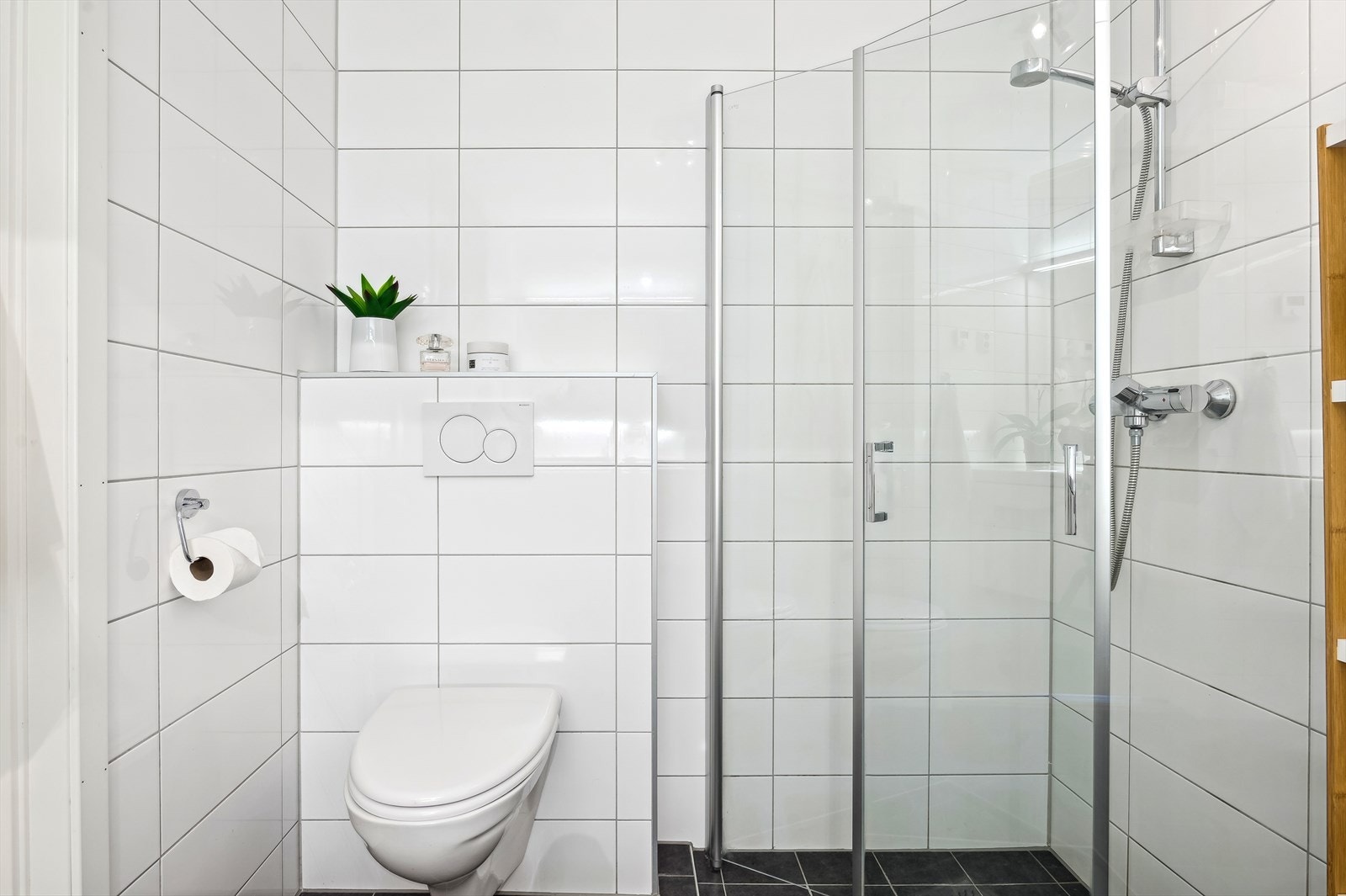 Baderomsinnredning bestående av benkeskap med glatte fronter, speil/belysning over servant, dusj på gulv med innfellbare dører i herdet glass, servant i helstøpt plate og veggfestet klosett. Galleribilde