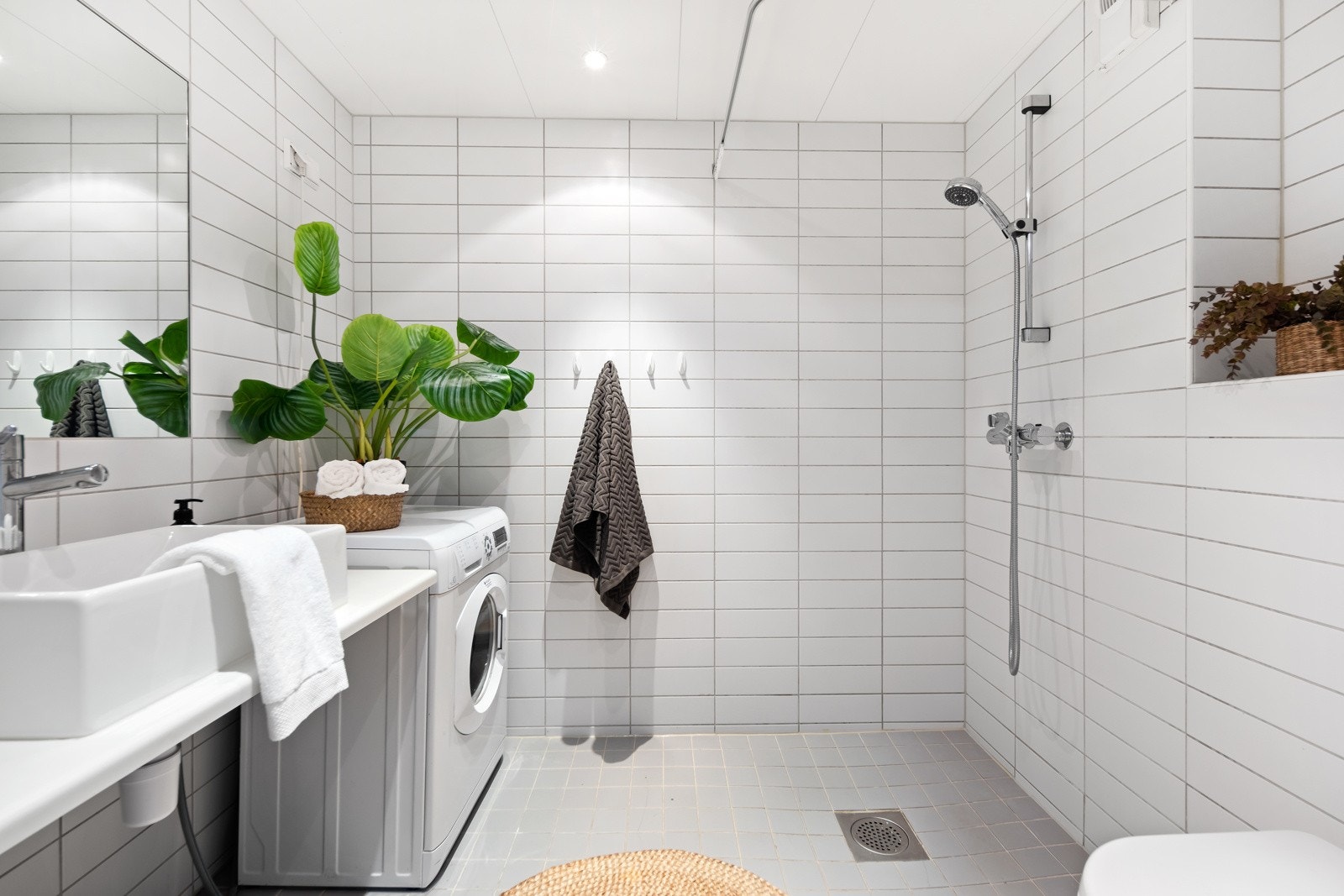 Lyst, flislagt baderom innredet med dusj, servant, klosett og opplegg for vaskemaskin. Galleribilde