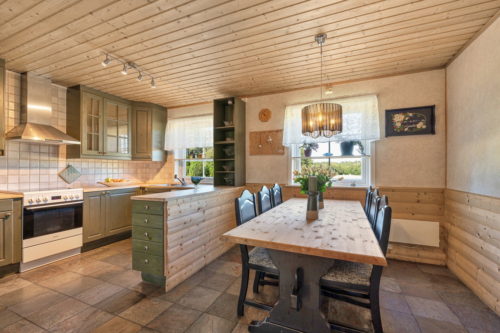 Kjøkkenet har fliser på gulvet, takhøy innredning, stilig barløsning og plass til stort spisebordsmøblement. Galleribilde