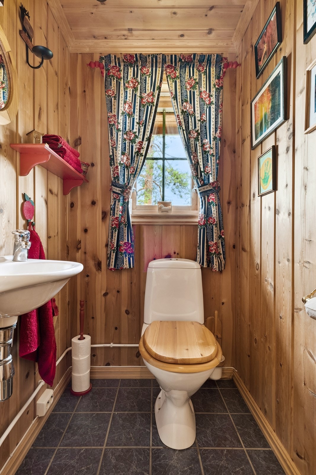 Toalettrom med panel på veggene og blå/grå fliser på gulvet. Rommet er innredet med servant montert på vegg og gulvmontert toalett. Galleribilde