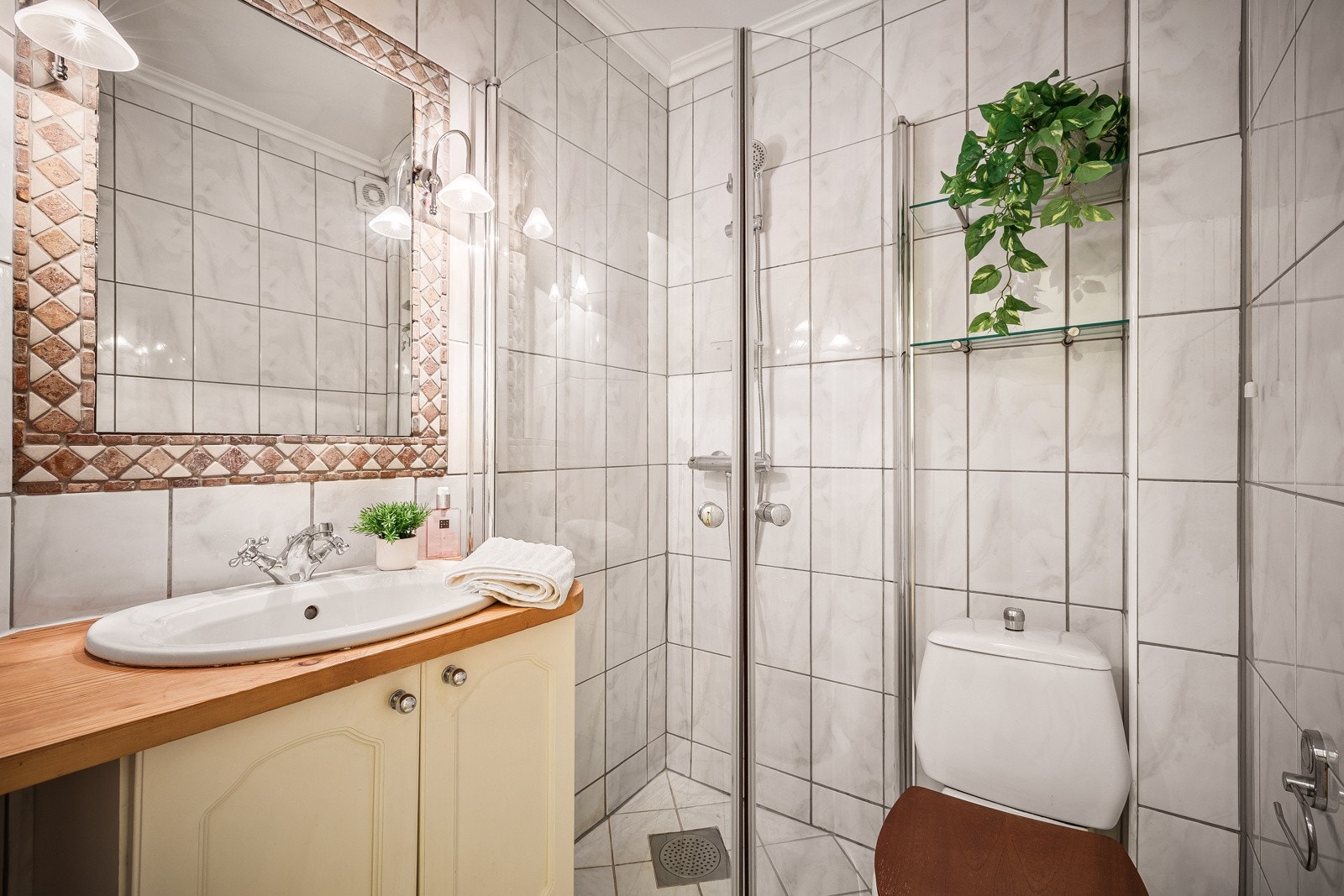 Badet har fliser på gulv- og veggflater og inneholder gulvmontert toalett, benkeskap med servant og dusjdører i glass. Galleribilde