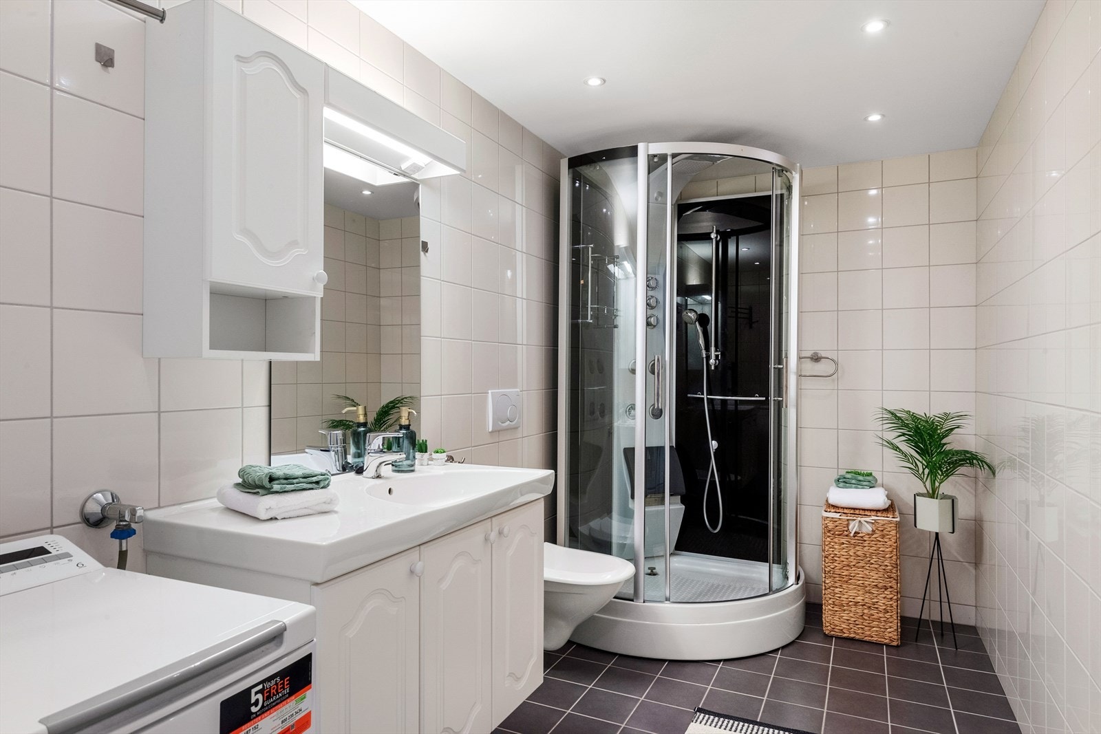 Innredningen på badet er innholdsrik med skap både på siden og under servanten. Et stort speil med integrert lys over danner en fin helhet. Badet har vegghengt toalett, dusjkabinett og opplegg for vaskemaskin. Det er vannbåren varme i gulvet. Galleribilde