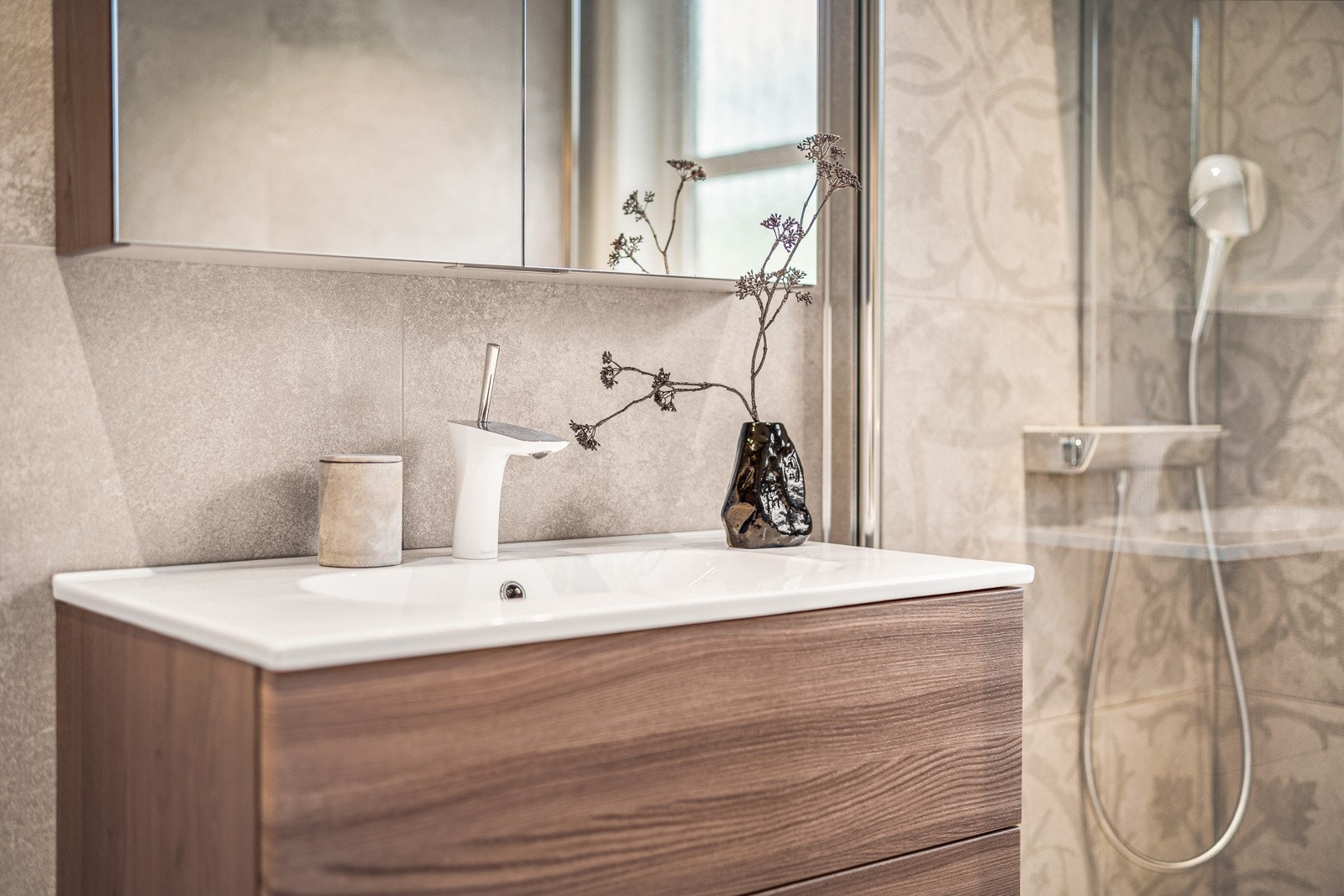 Badet er innredet med vegghengt toalett, dusj med glass foldedører, servant med møblement, speil og belysning. Galleribilde