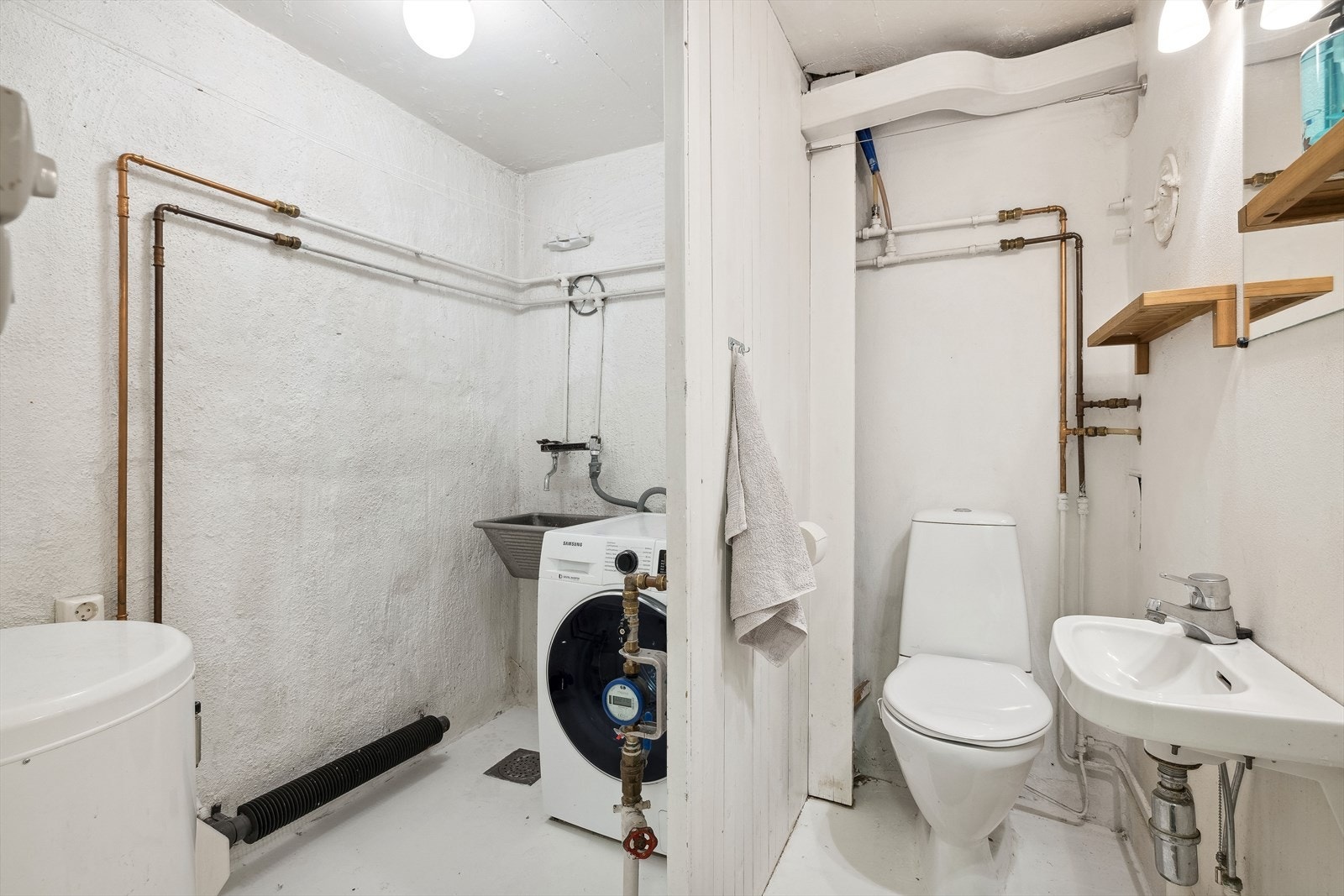 Eget vaskerom med malte muroverflater. Vaskerommet er innredet med utslagsvask i stål, gulvstående wc, enkel servant, samt opplegg og plass til vaskemaskin Galleribilde