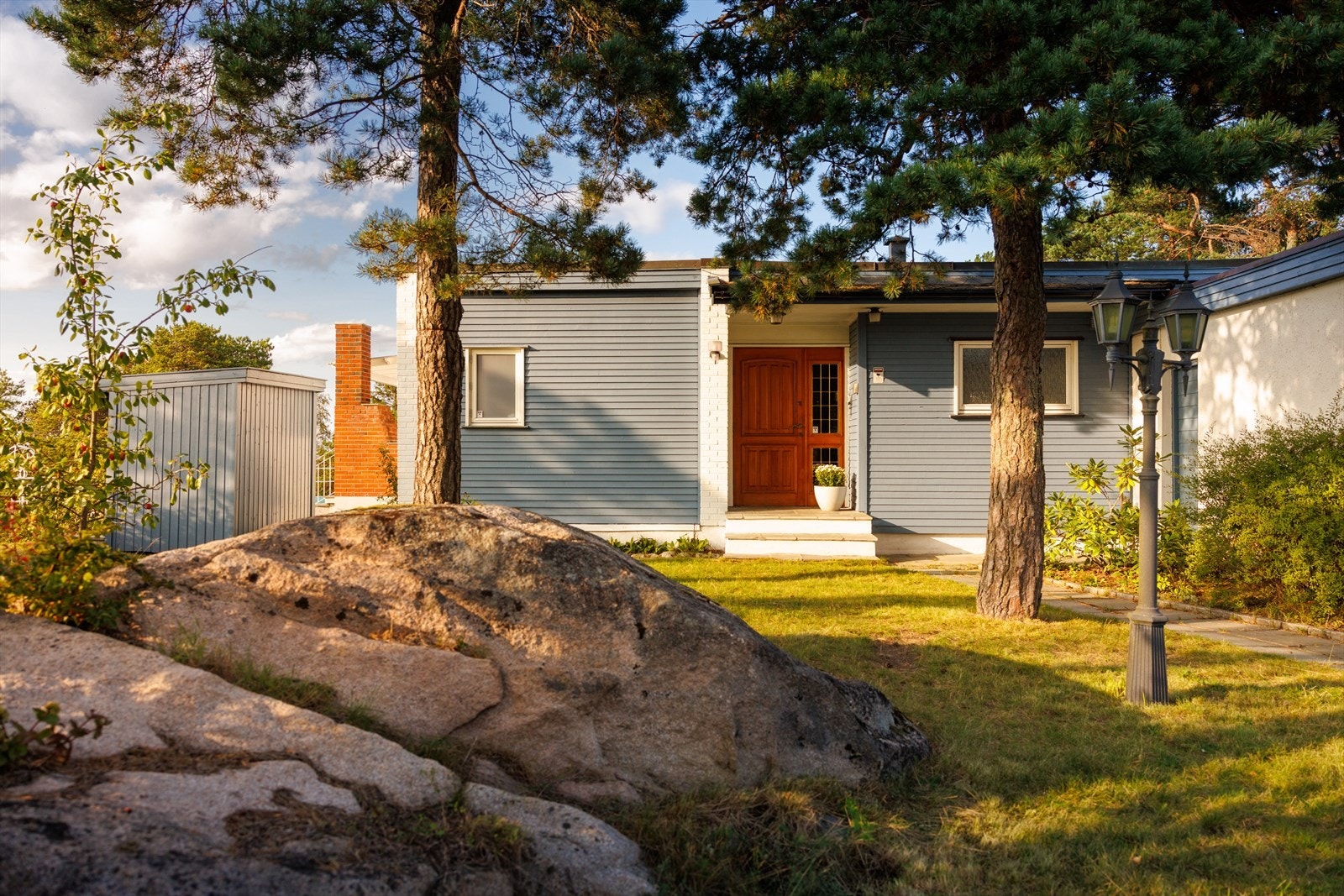 Forbi smijernsporten leder en ganske lang innkjørsel opp til garasjen. Huset som liksom skjuler seg bak, flankert av løvtrær og furu. Galleribilde