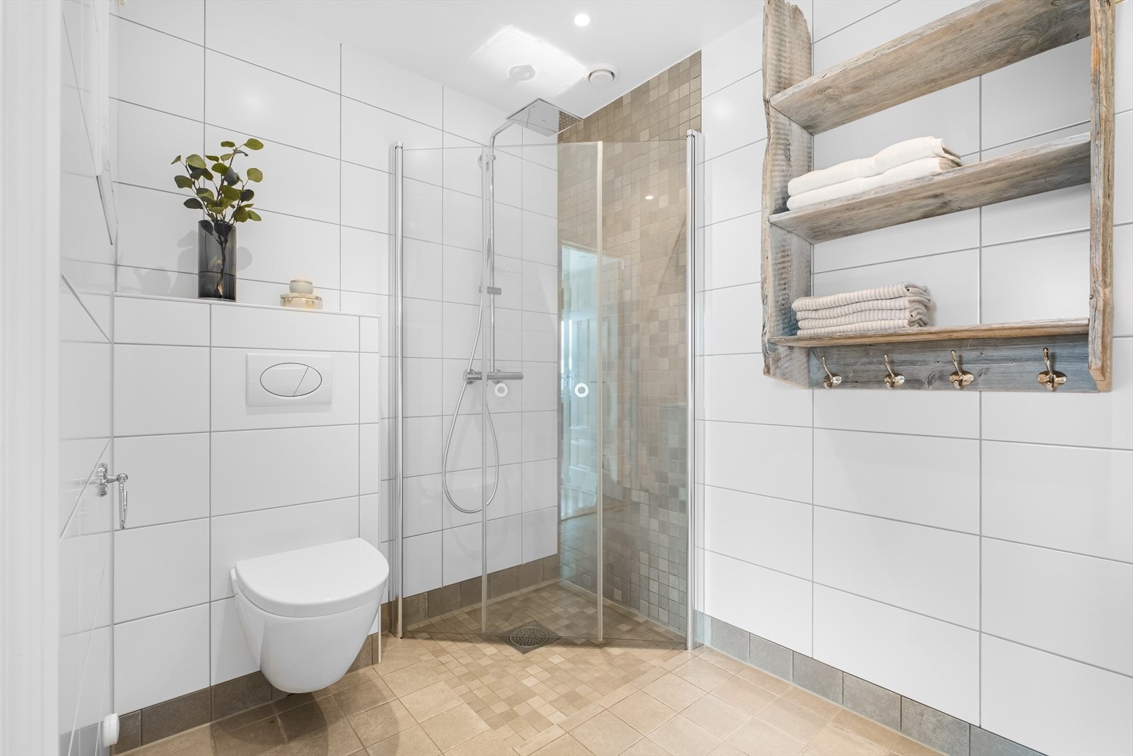 Stort og lekkert bad fra 2014 med fliselagte overflater og varmekabler i gulv. Badet er innredet med vegghengt toalett og regnfallsdusj med svingbare dører i nedsenket sone. Galleribilde