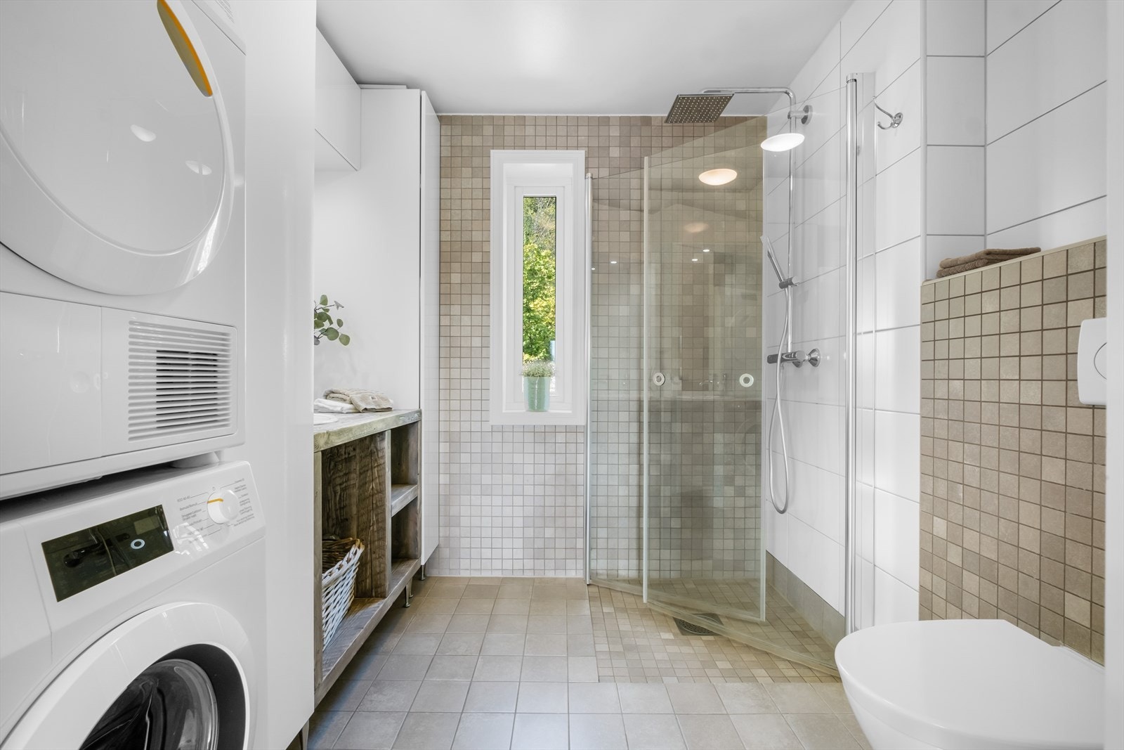 Lyst og stilrent bad fra 2014 med flislagte overflater og varmekabler i gulv. Badet er innredet med vegghengt toalett, regnfallsdusj med svingbare dører i nedsenket sone, håndlaget og eksklusiv servant og innredning, samt speil og lys i rommet. Galleribilde