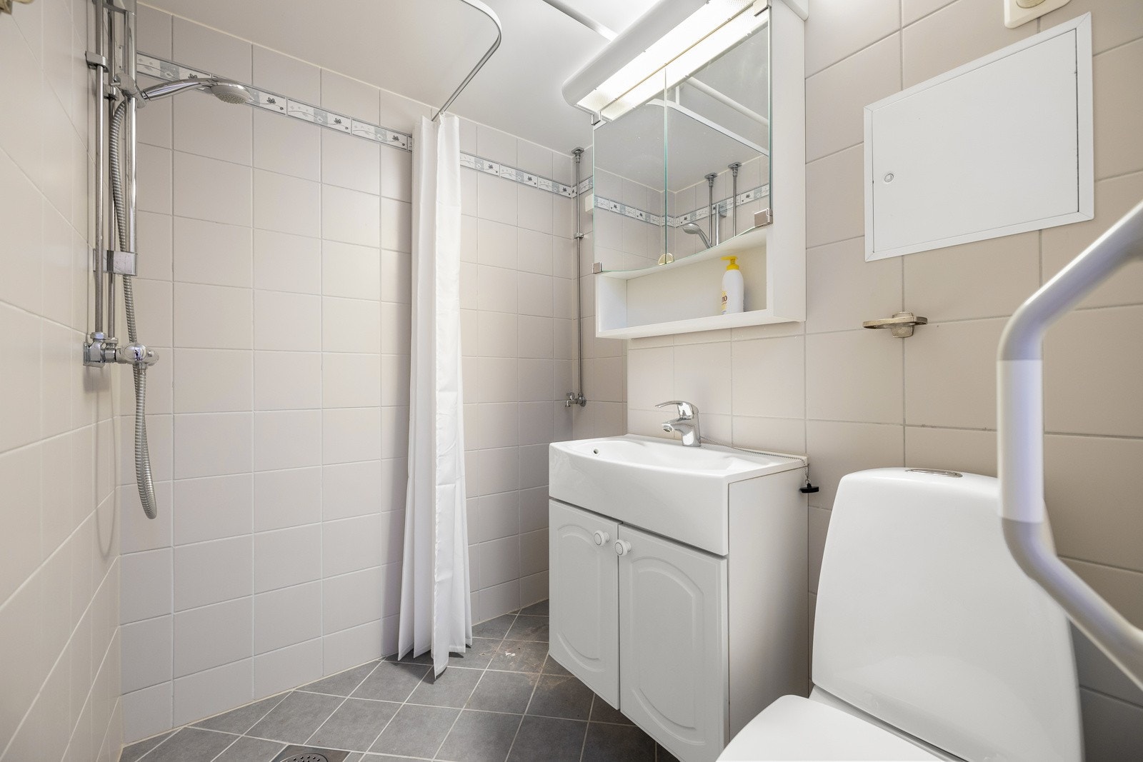 Badet er utført med vegghengt servantinnredning med ett-greps armatur, speilskap med stikkontakt og overlys, gulvstående toalett, samt dusjhjørne med forheng. Galleribilde