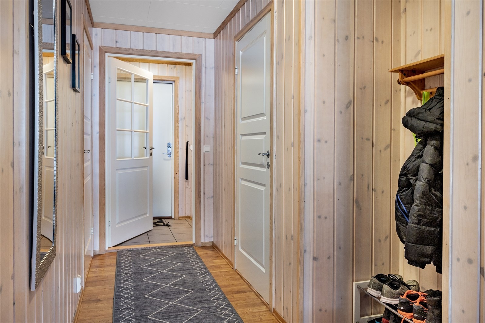 Entré bestående av fliser på gulv, panel på vegger og plater i himling. Det er dør inn til gangen, hvor det er plass til å henge fra seg yttertøy eller etablere en garderobeløsning. Her er det parkett på gulvet. Galleribilde