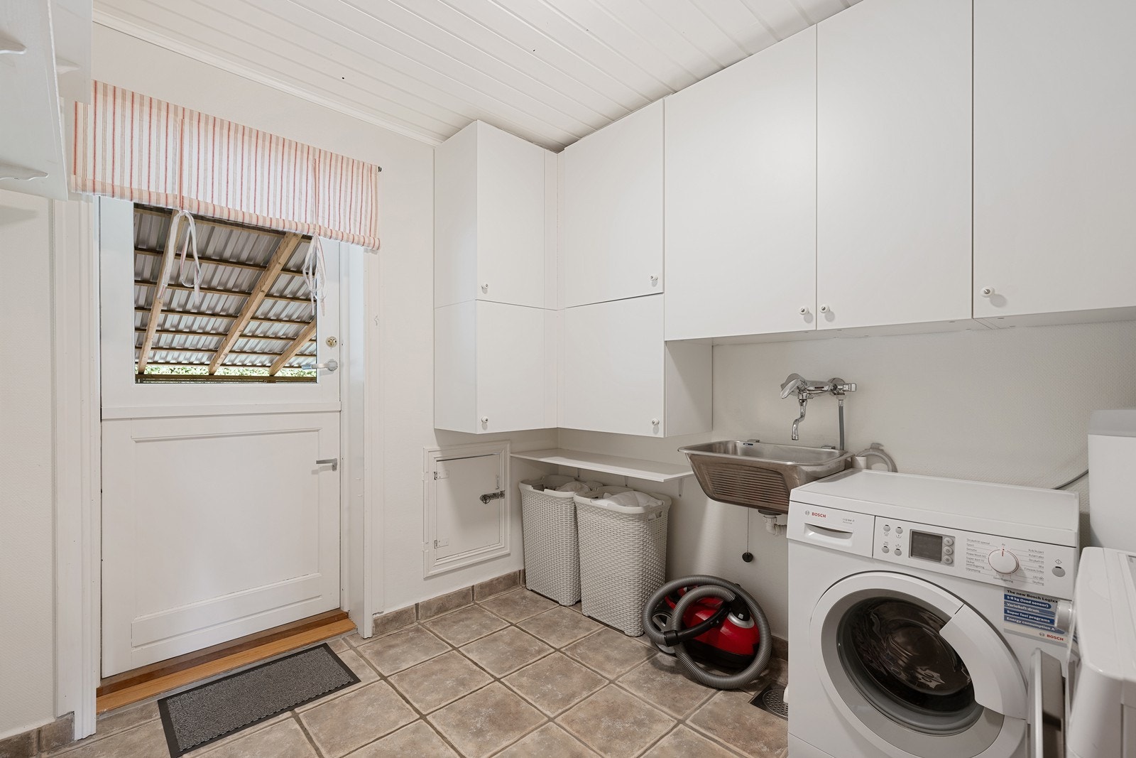 Vaskerommet har mye skapplass, skyllekum i stål, varmekabler og gulvfliser med sokkelflis. Galleribilde