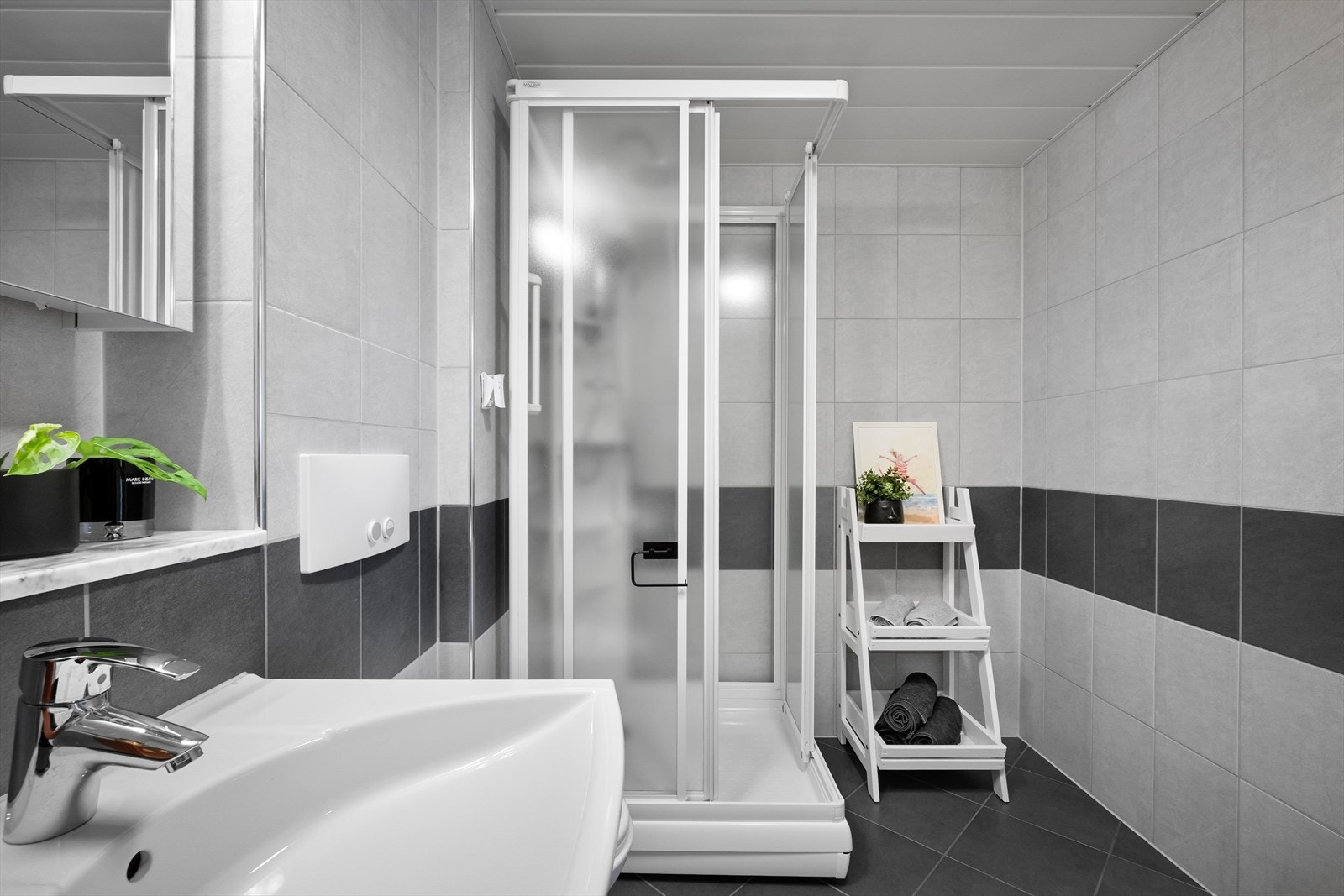 Badet inneholder dusjkabinett, opplegg for vaskemaskin, servantskap, speilskap og veggfestet wc. Galleribilde