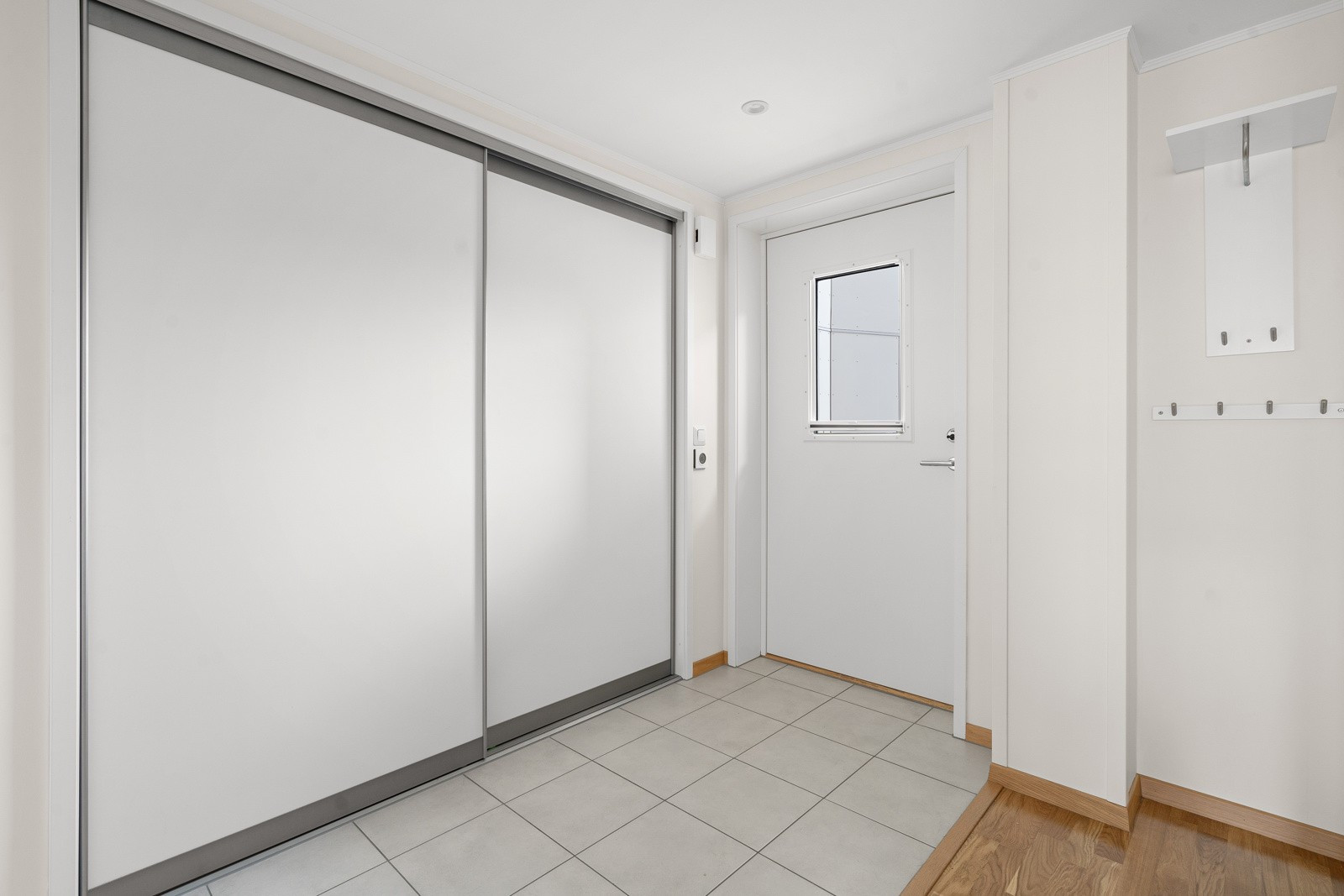 Flislagt inngangsparti med stor skyvedørsgarderobe som sikrer godt med oppbevaringsplass til yttertøyet.