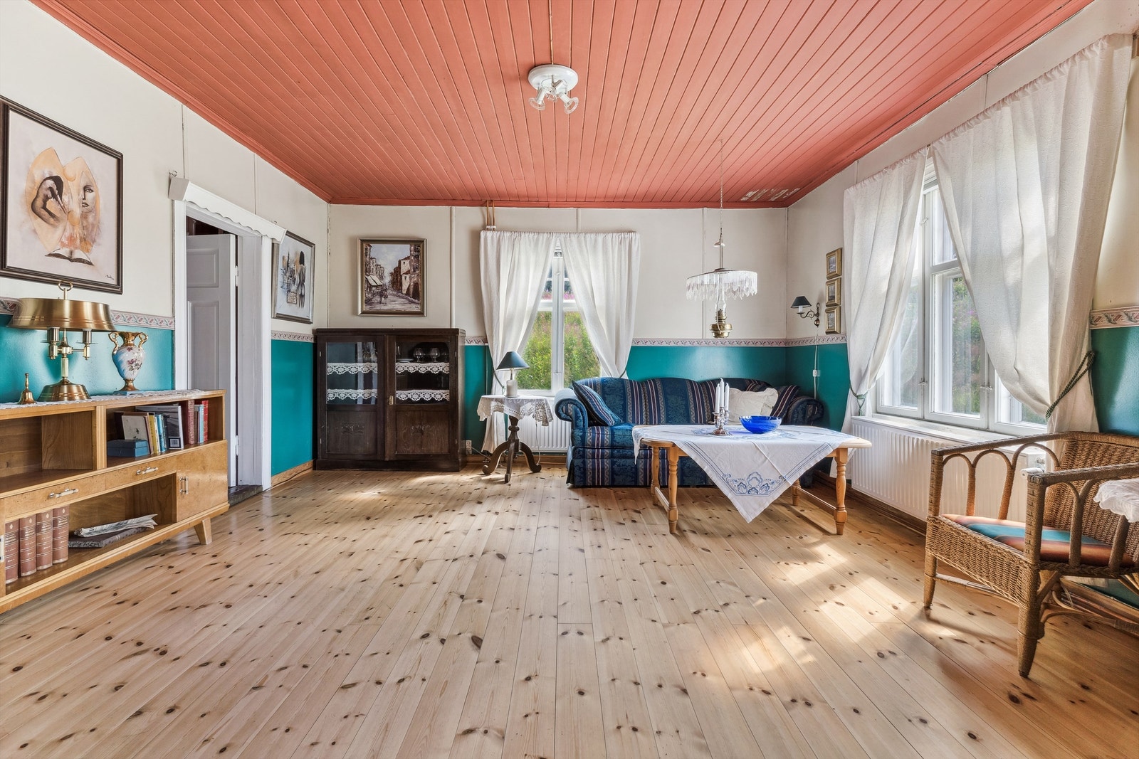 Stuen har blå/grønn og hvitmalte vegger, furugulv og rødmalt panel i himling. Galleribilde