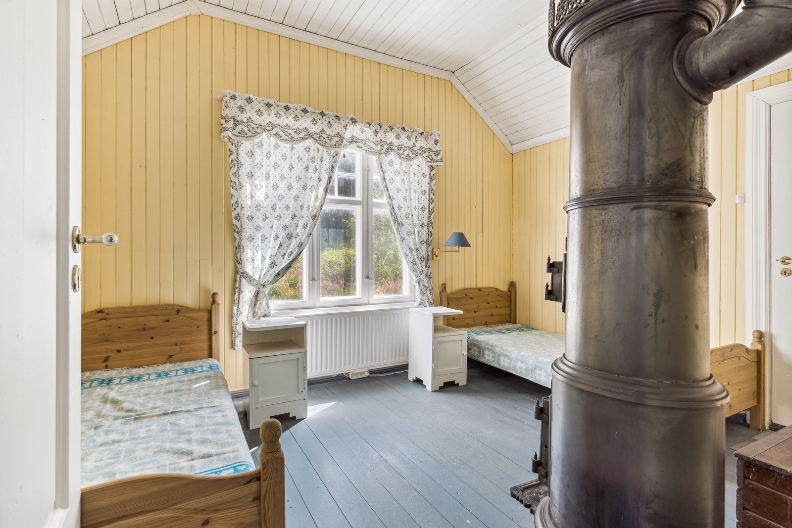 Det tredje soverommet har gulmalt panel på veggene og blåmalt furugulv. Rommet er romslig med god plass til senger, nattbord og annet soveromsmøblement. Dette rommet har en gammel vedovn etablert i rommet. Galleribilde