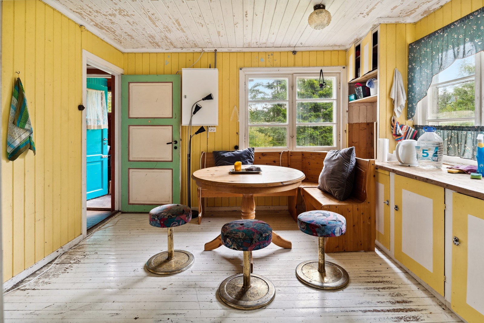 Kjøkken med gulmalt panel på veggene, hvitt og slitt panel i himling og hvitmalt tregulv. Kjøkkenet er innredet med plassbygd innredning med underskap, en skuffeseksjon, benkeplate og ett dobbelt overskap. Galleribilde