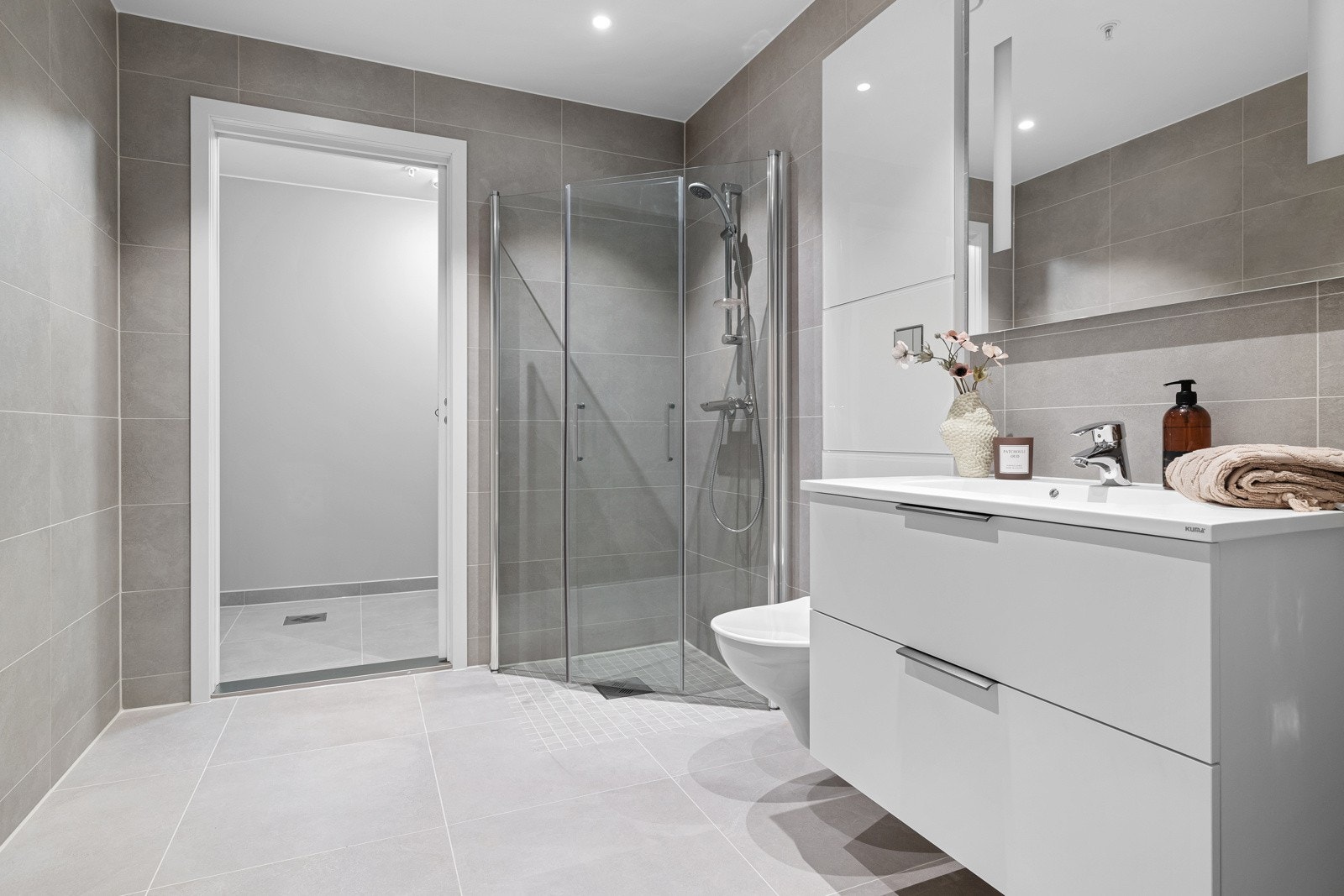 Videre er badet utstyrt med veggmontert toalett og dusjhjørne med innfellbare dusjdører i glass. Galleribilde