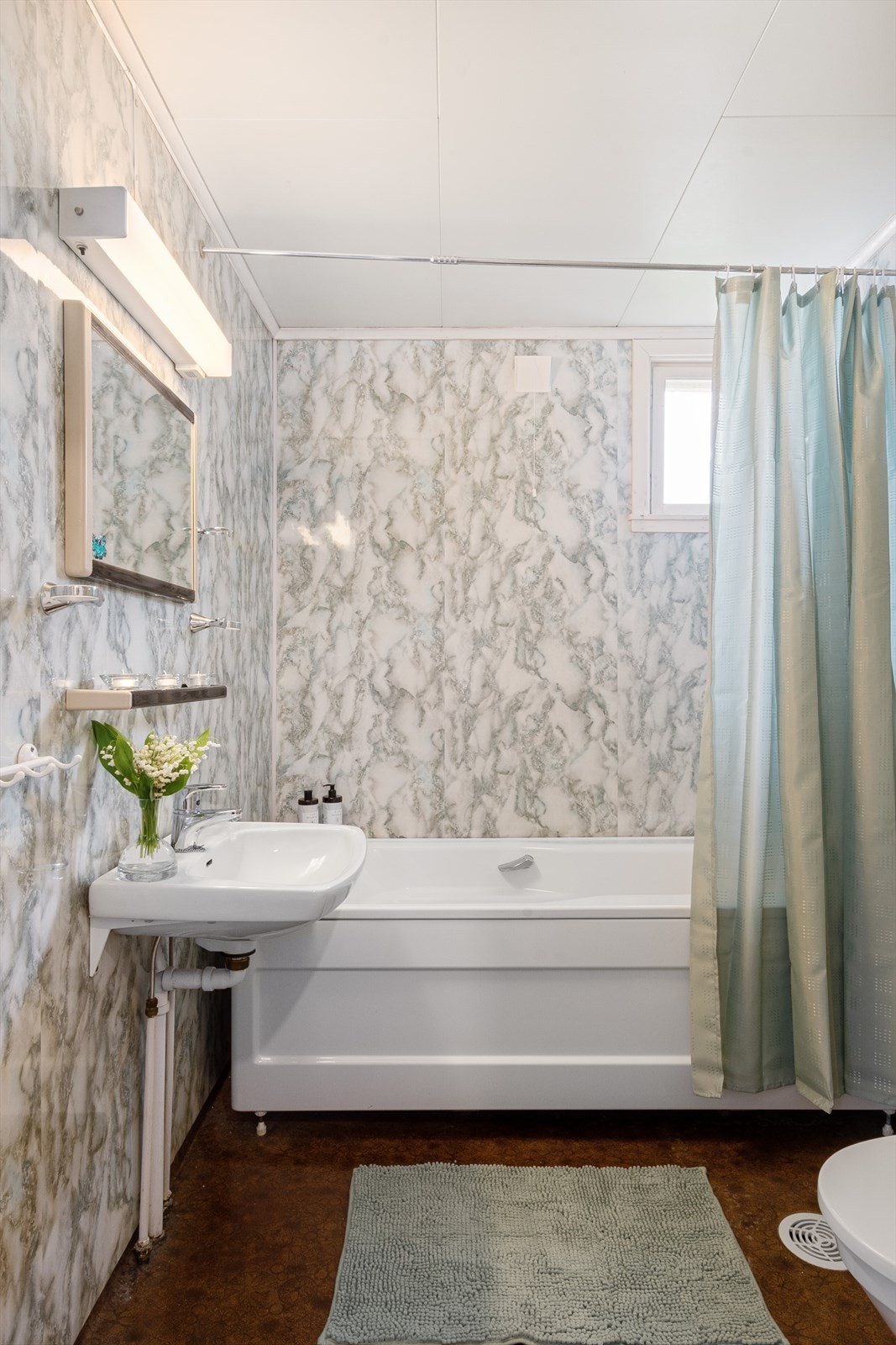 Baderommet har spraglete våtromsplater på veggene og spraglete mørkt belegg på gulvet. Galleribilde