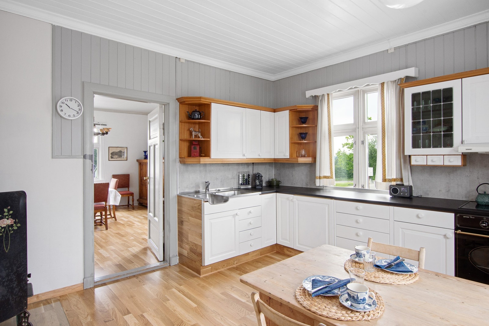 Kjøkkeninnredning med hvite heltre profilerte fronter, laminerte skrog og laminerte benkeplater. Innredningen består av over- og underskap, høyskap og skuffer, ett overskap med vitrinedør. Galleribilde