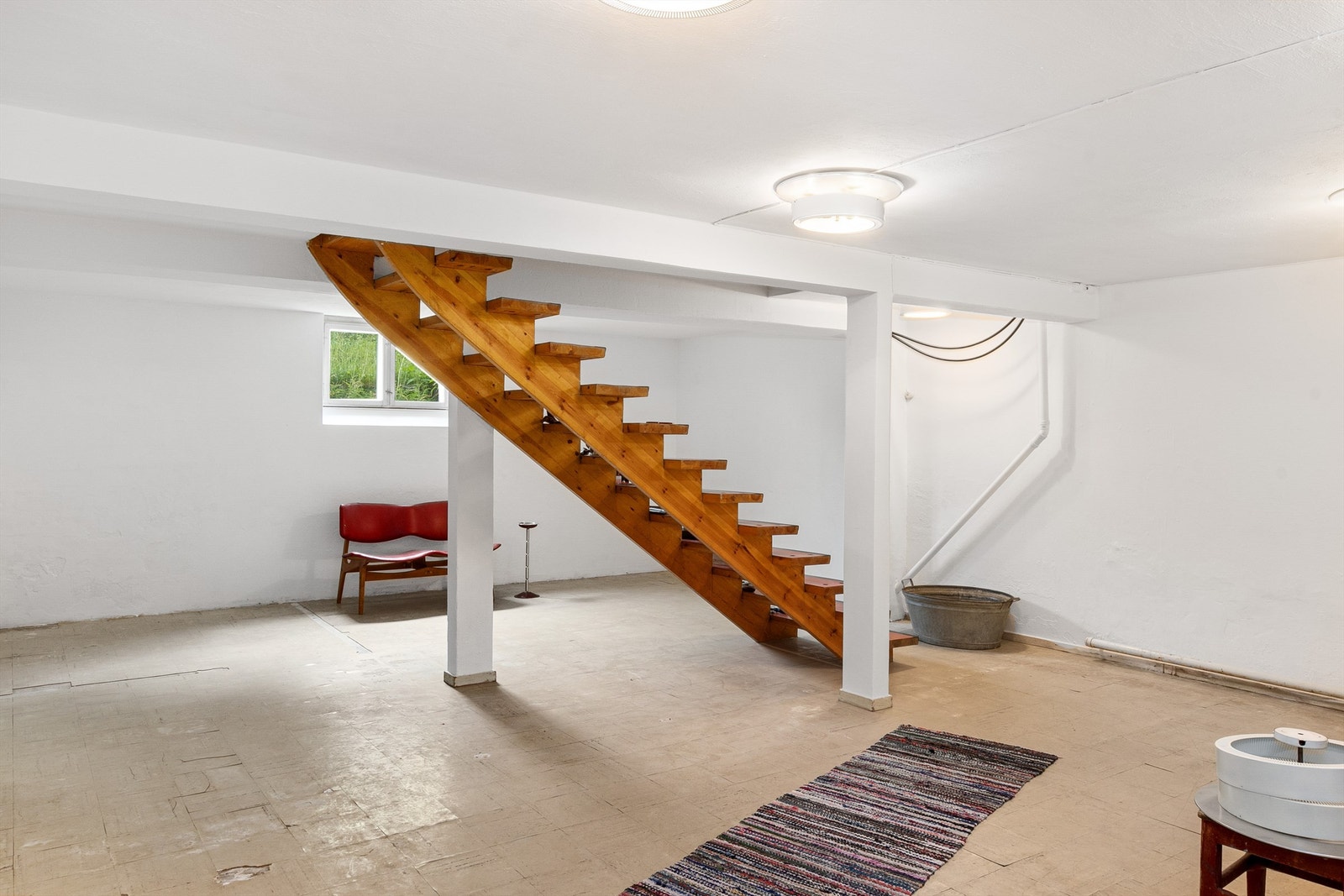 Kjeller med hvitmalt betong på veggene og belegg på gulvet. Kjellertrappen kommer ned midt i rommet, og har ikke rekkverk/gelender. Galleribilde