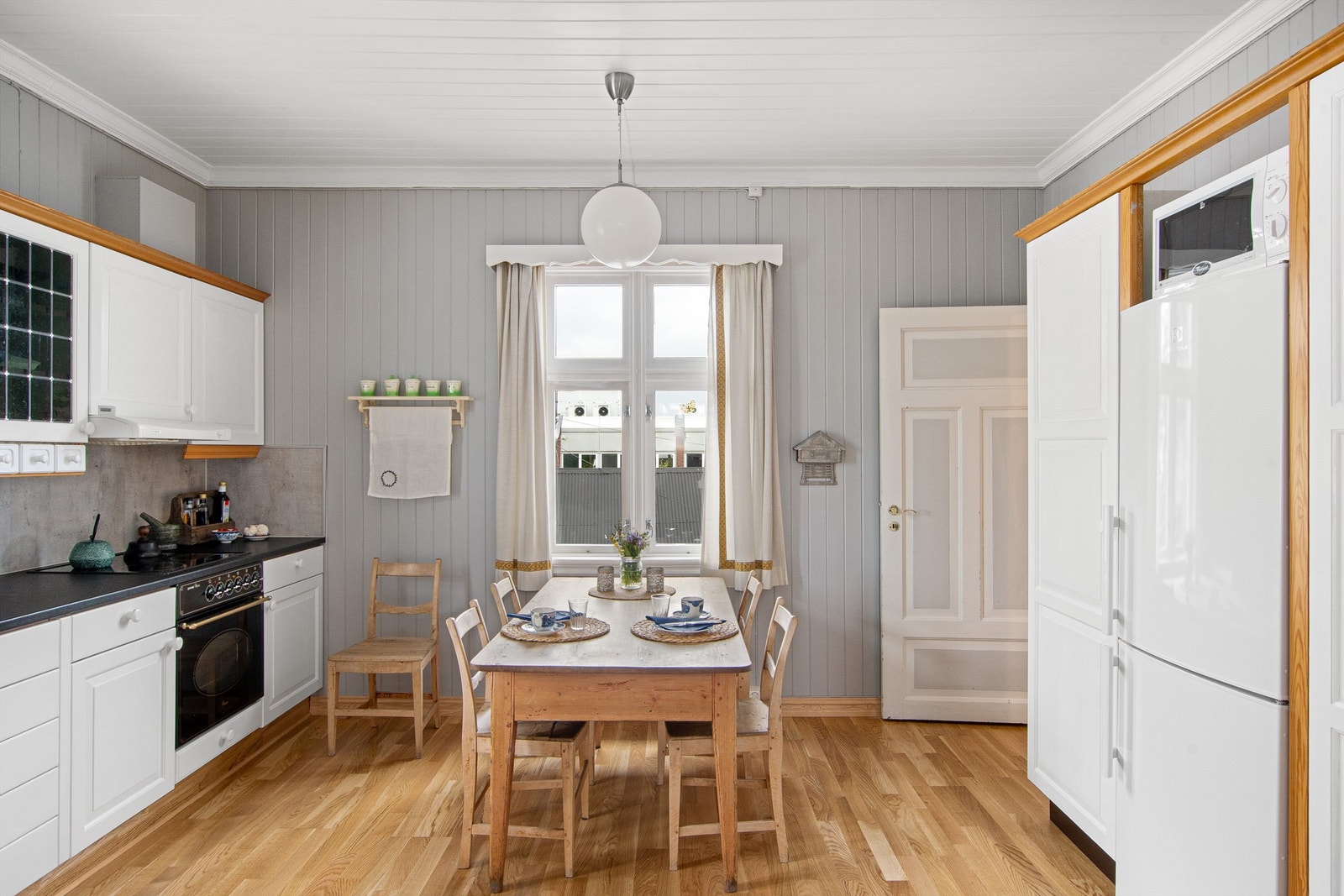 Veggflatene over kjøkkenbenk med grå plater med betongutseende. Integrerte hvitevarer som komfyr og platetopp er etablert, samt åpen løsning for kjøl-/fryseskap og opplegg for oppvaskmaskin. Galleribilde