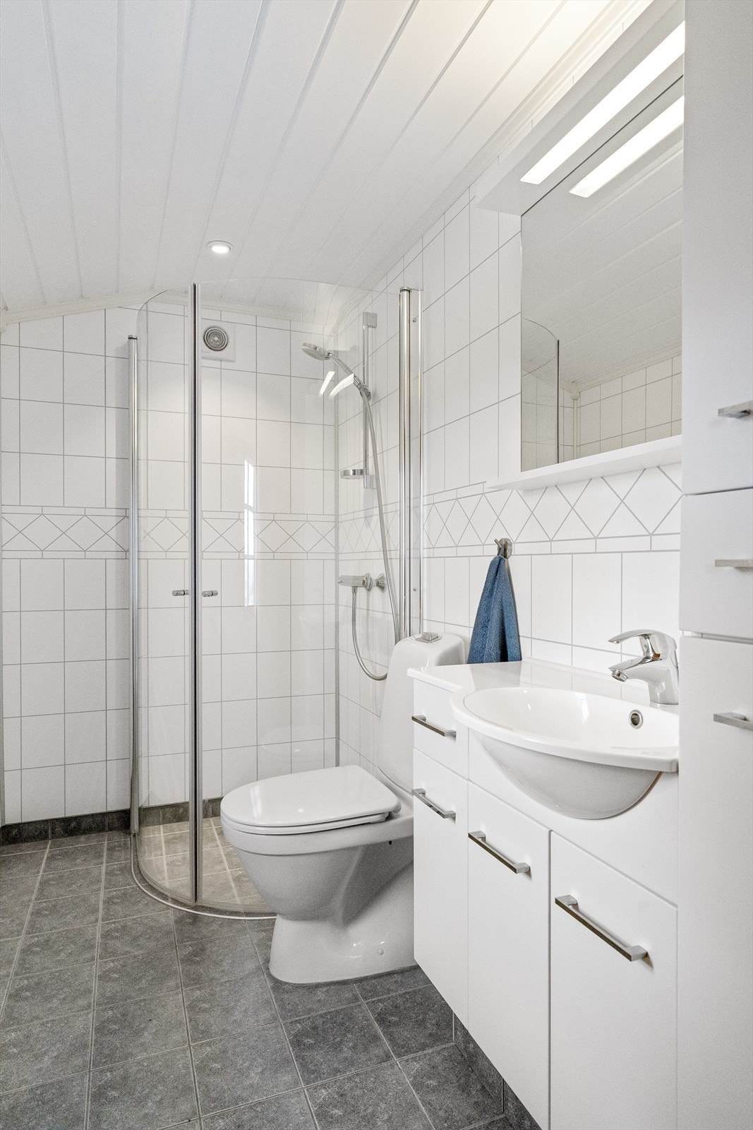 Her har man dusjhjørne med innfellbare glassvegger, vanlig vannklosett, og en romslig baderomsinnredning med speil og god skapplass til. Galleribilde