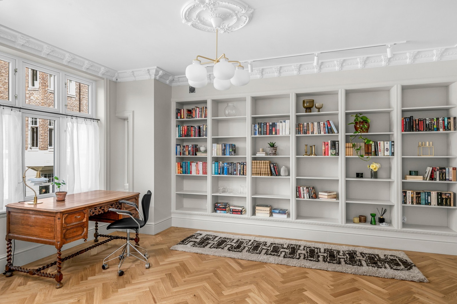 Biblioteket har plassbygde bokhyller flott innrammet med stukkatur. Også her rosett i tak og eikestaver i fiskebensmønster. Galleribilde