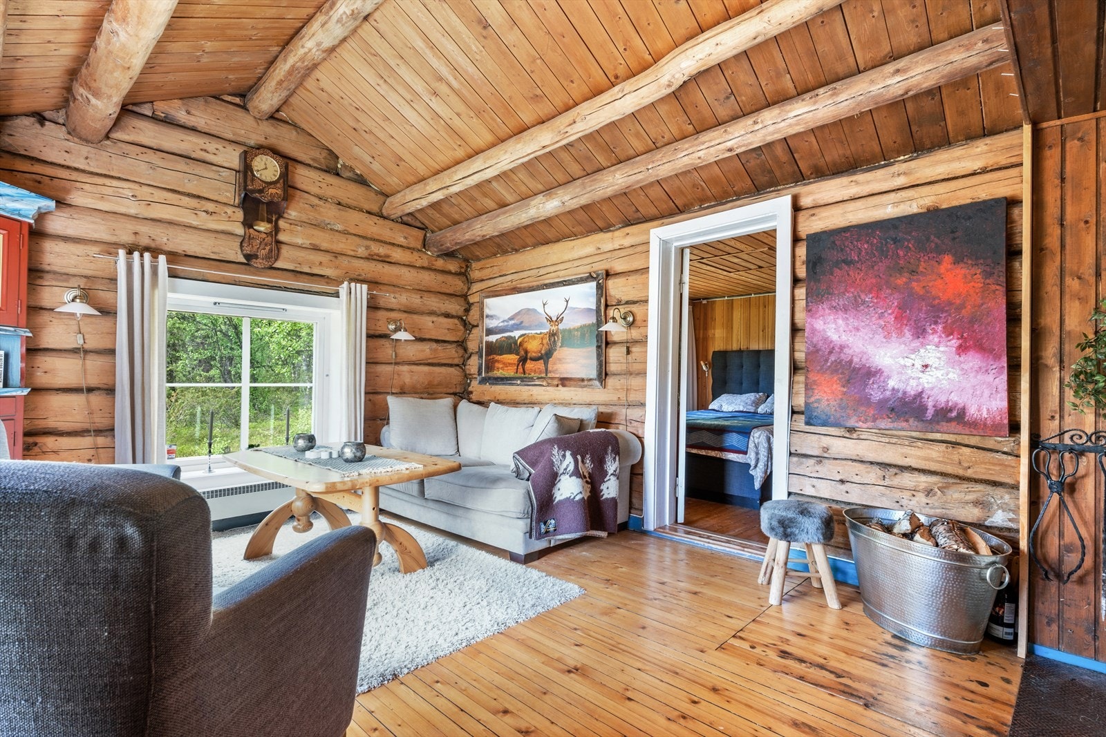 Meget trivelig stue med synlige tømmervegger, høy skråhimling med åser og peis med innsats. Galleribilde