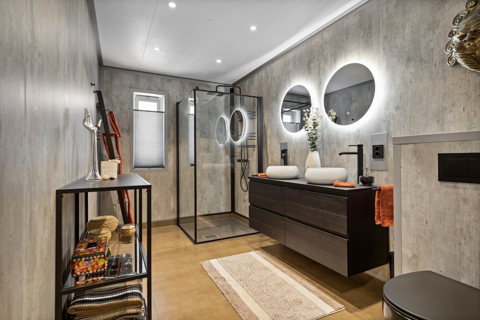 Badet er av moderne utførelse med fliser på gulvet og grå baderomsplater på veggene. Dusjsonen har fine glassdører i sort ramme, mosaikkfliser på gulvet og sort regnfallsdusj Galleribilde