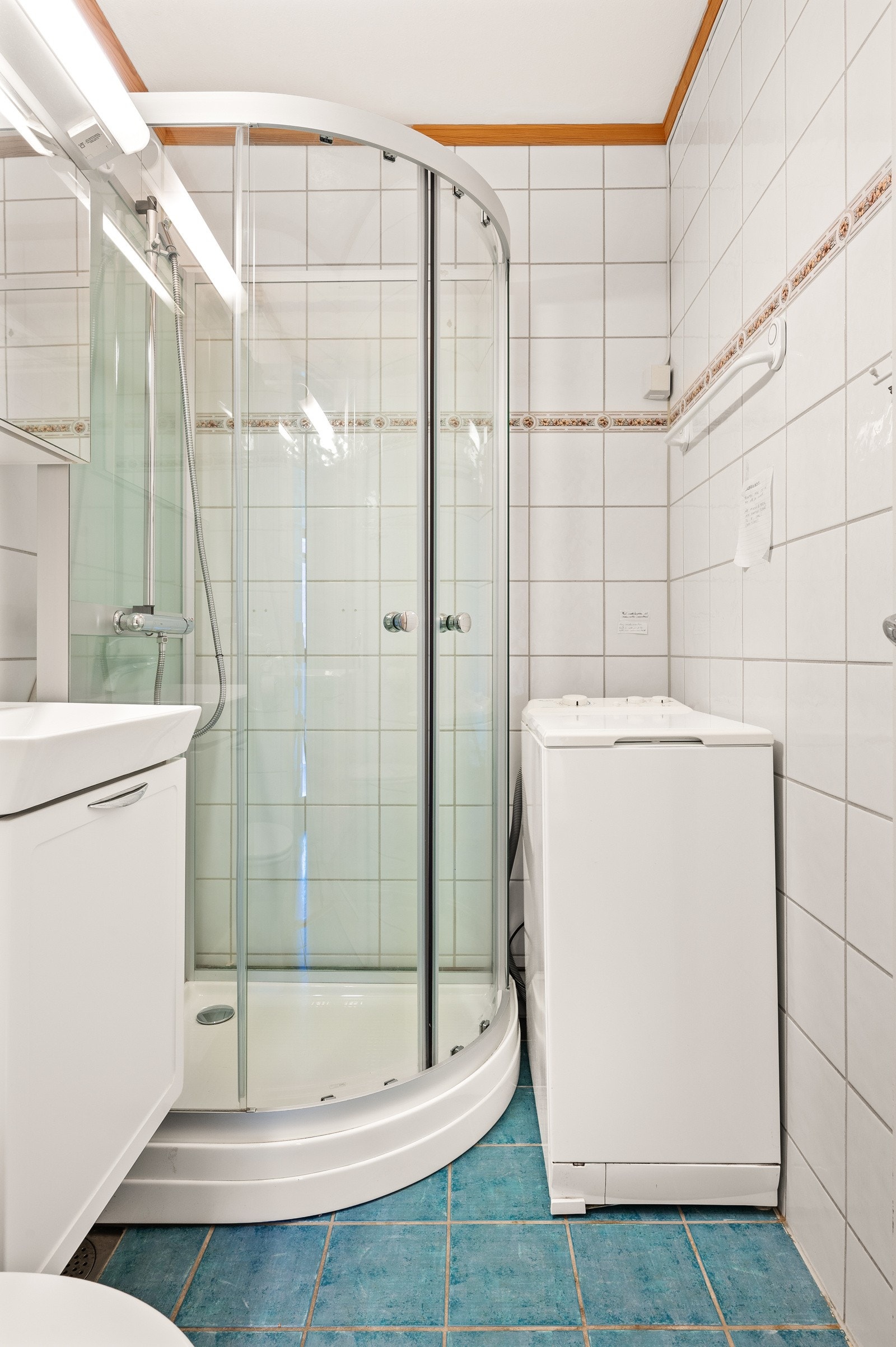 Badet har fliser på gulv og vegger, dusjkabinett, gulvstående toalett og opplegg for vaskemaskin. Galleribilde